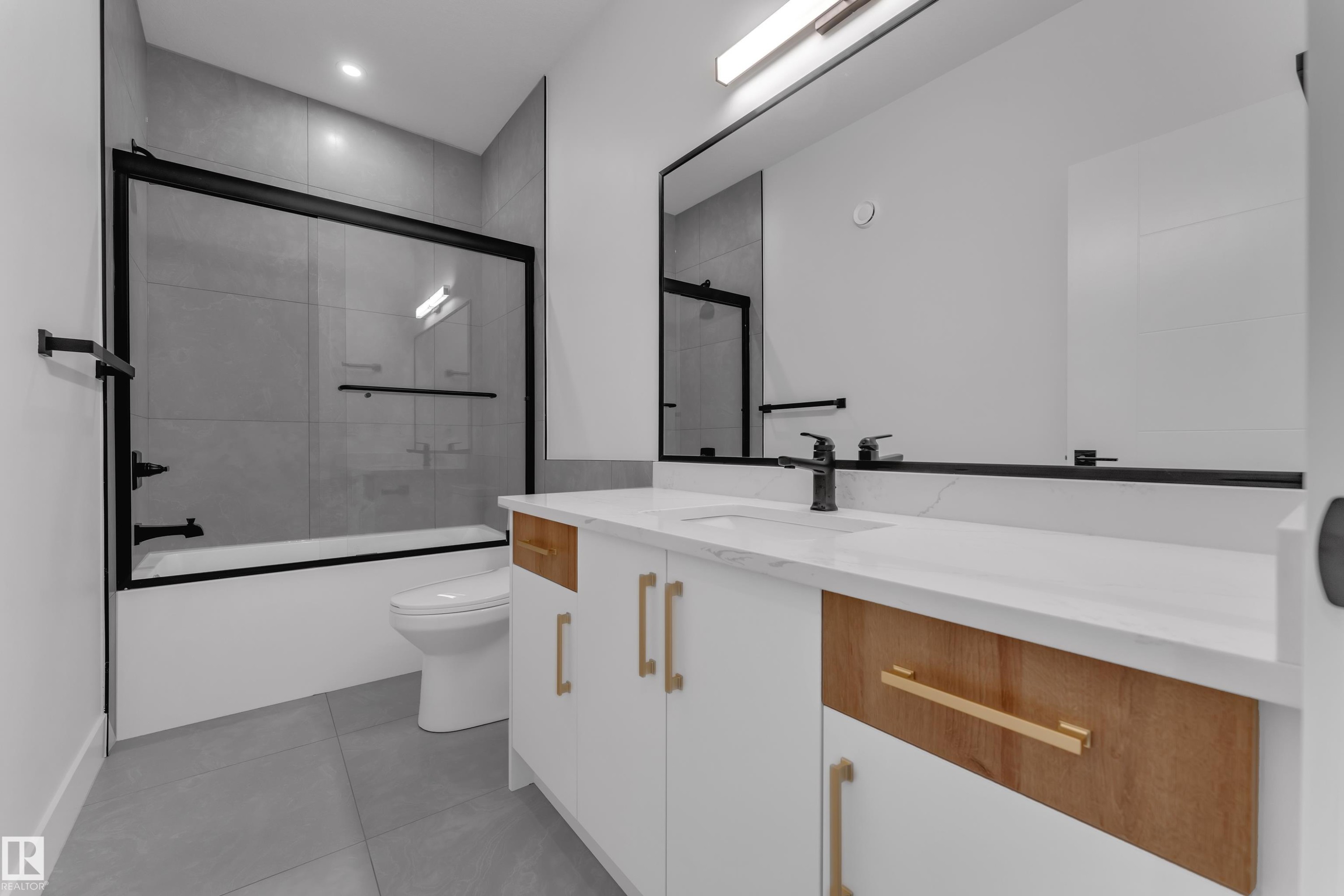 Bathroom featuring a vanity with a white countertop and gold-toned hardware, a rectangular mirror, and a bathtub with a sliding glass enclosure and black fixtures - 764 Astoria Way, Devon, AB - Indoor Photo Showing Bathroom