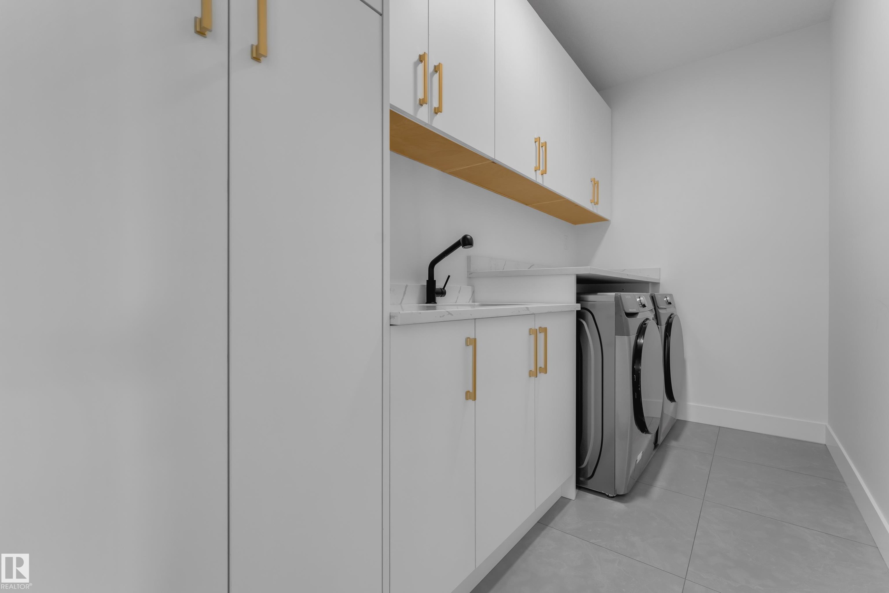 Built-in white cabinetry with gold-tone hardware, wood-finish shelving, and a sink with a matte black faucet - 764 Astoria Way, Devon, AB - Indoor Photo Showing Laundry Room