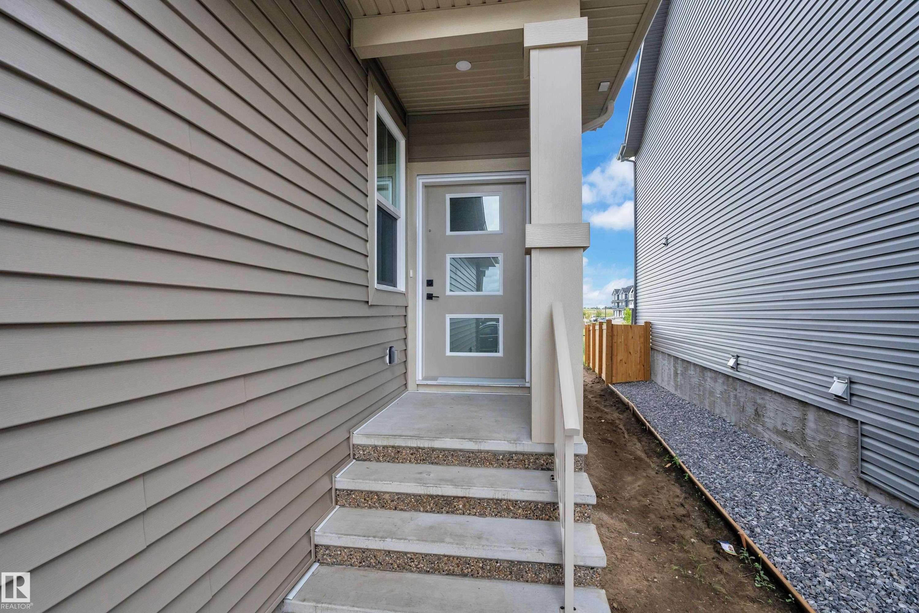 Modern entry door with three frosted glass panels, concrete steps with exposed aggregate risers, and a covered porch supported by a substantial column - 764 Astoria Way, Devon, AB - Outdoor With Exterior