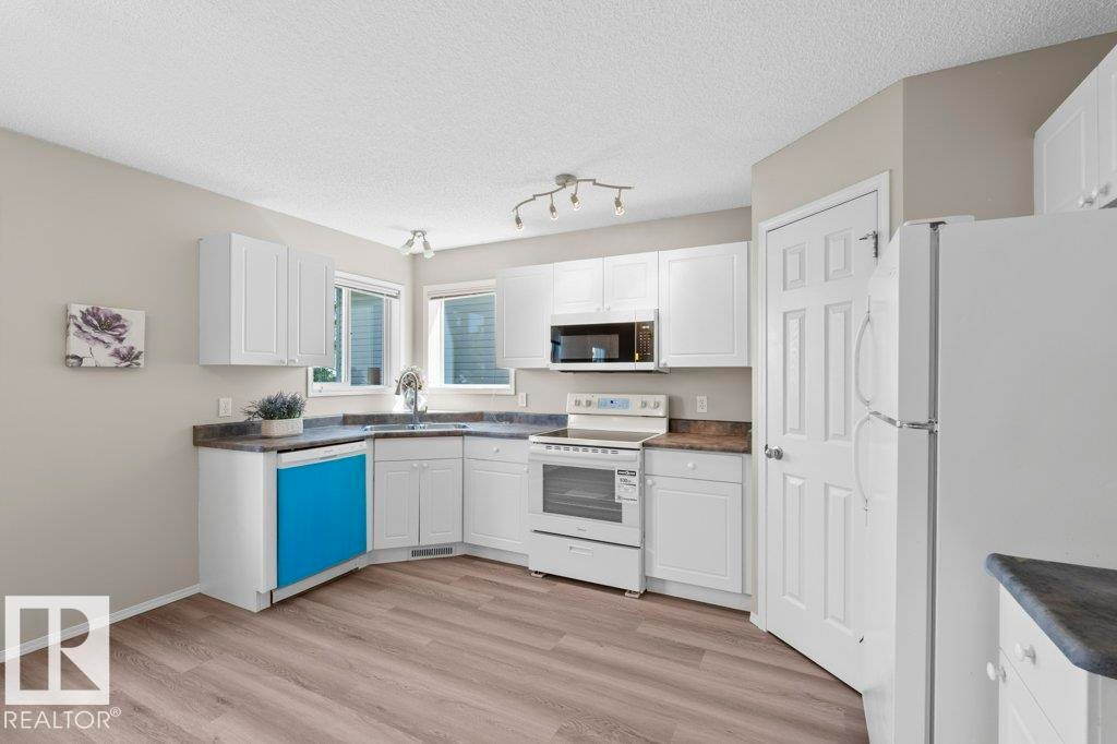 Kitchen featuring white cabinetry, wood-finish flooring, a stainless steel sink, and a built-in microwave - 21344 88 Avenue Nw, Edmonton, AB - Indoor Photo Showing Kitchen