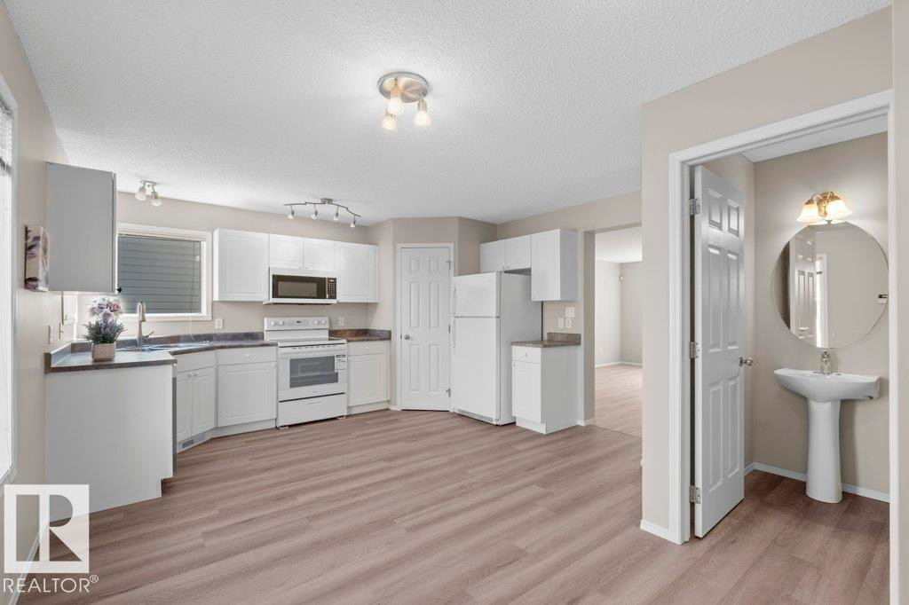 Kitchen featuring white cabinetry, white appliances, dark countertops, and wood-finish flooring - 21344 88 Avenue Nw, Edmonton, AB - Indoor Photo Showing Kitchen