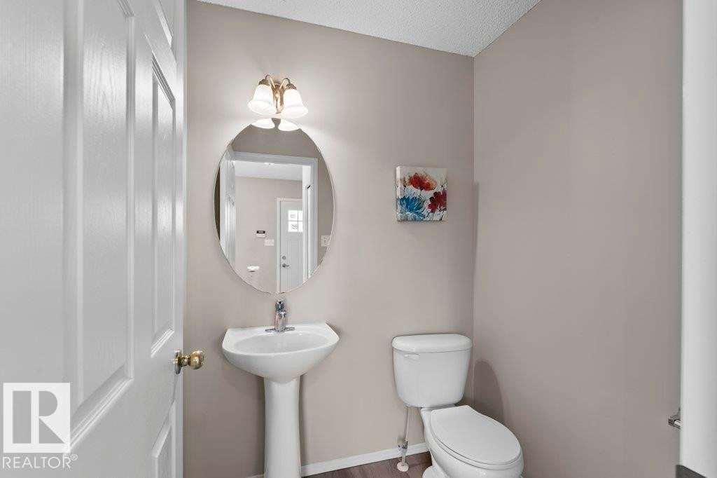 Pedestal sink with an oval mirror and two-light vanity fixture - 21344 88 Avenue Nw, Edmonton, AB - Indoor Photo Showing Bathroom