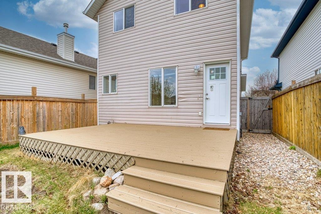 Rear exterior featuring a spacious composite deck with lattice skirting and wood stairs, a white rear entry door, and light-colored vinyl siding - 21344 88 Avenue Nw, Edmonton, AB - Outdoor With Exterior
