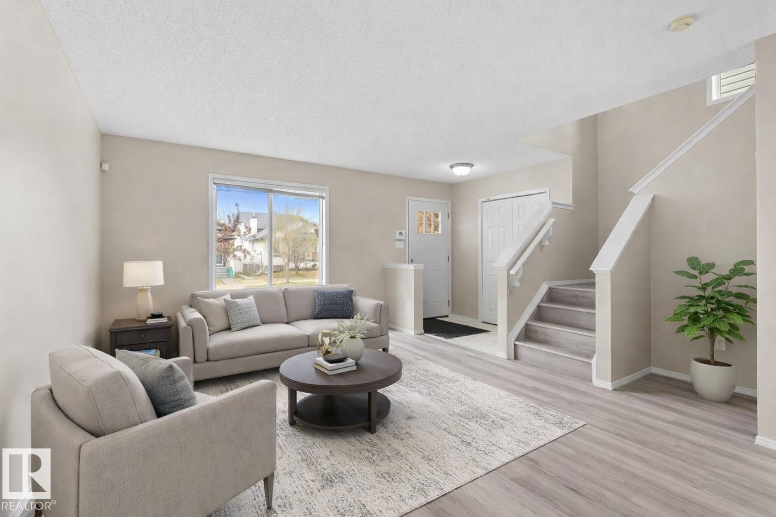 Open-concept living area featuring light wood-finish flooring, a contemporary staircase with white risers and handrails, and a front entry door with decorative glass inserts - 21344 88 Avenue Nw, Edmonton, AB - Indoor Photo Showing Living Room
