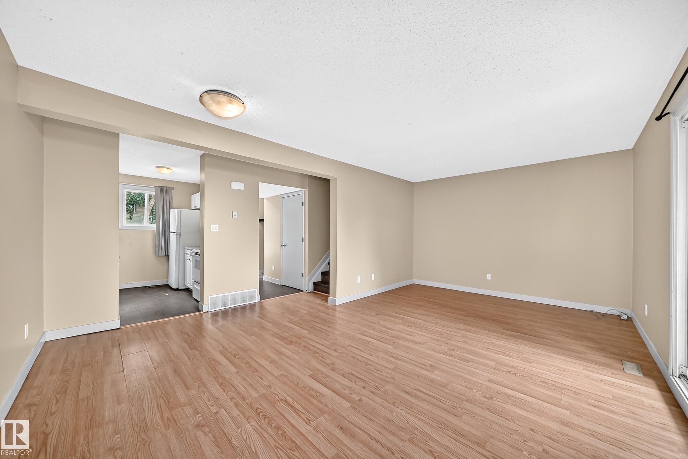 Spacious open-concept room featuring wood-finish flooring and neutral wall tones - 6416 180 Street Nw, Edmonton, AB - Indoor Photo Showing Other Room
