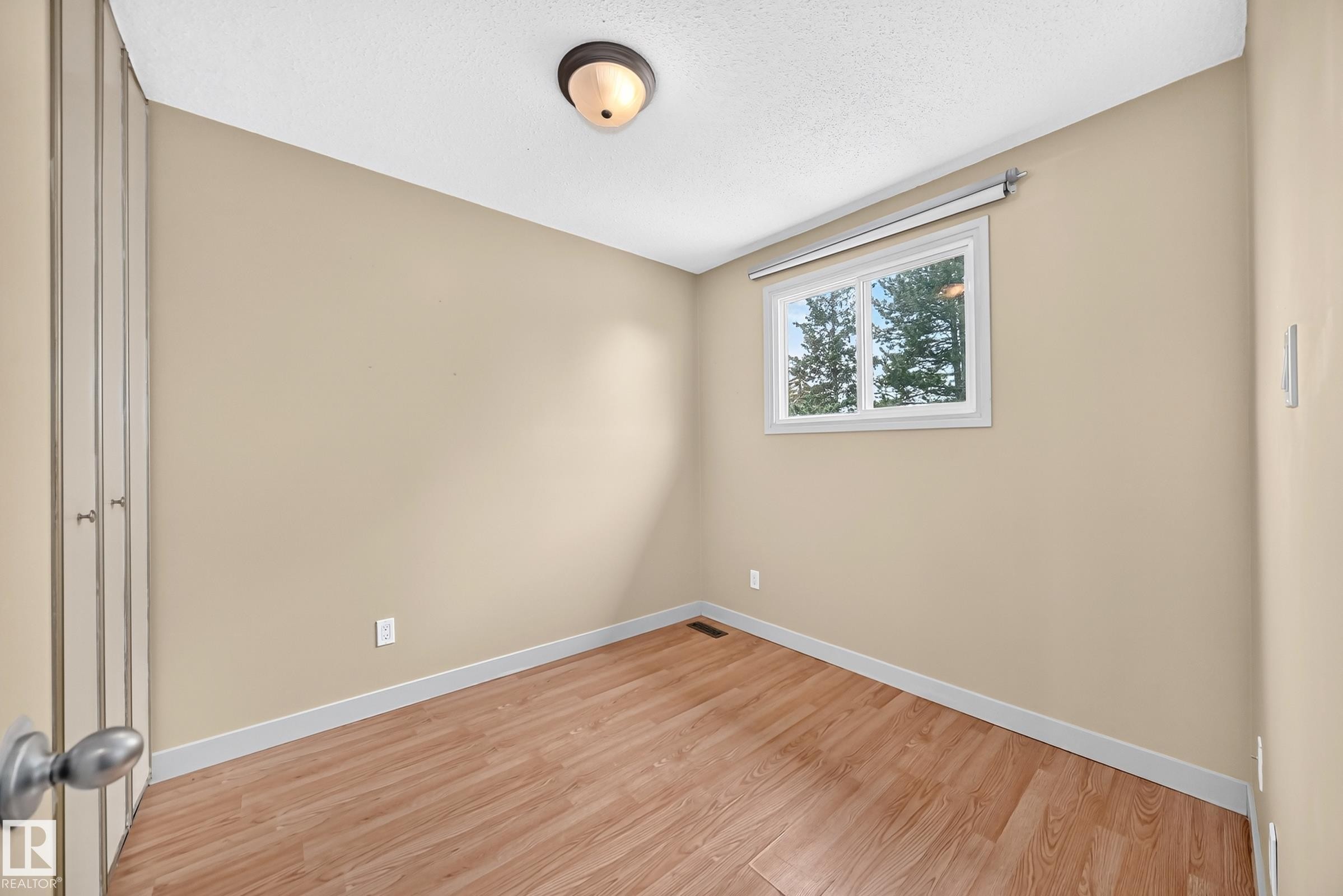 Wood-finish flooring, single window with white trim, flush mount ceiling light, and bi-fold closet doors - 6416 180 Street Nw, Edmonton, AB - Indoor Photo Showing Other Room