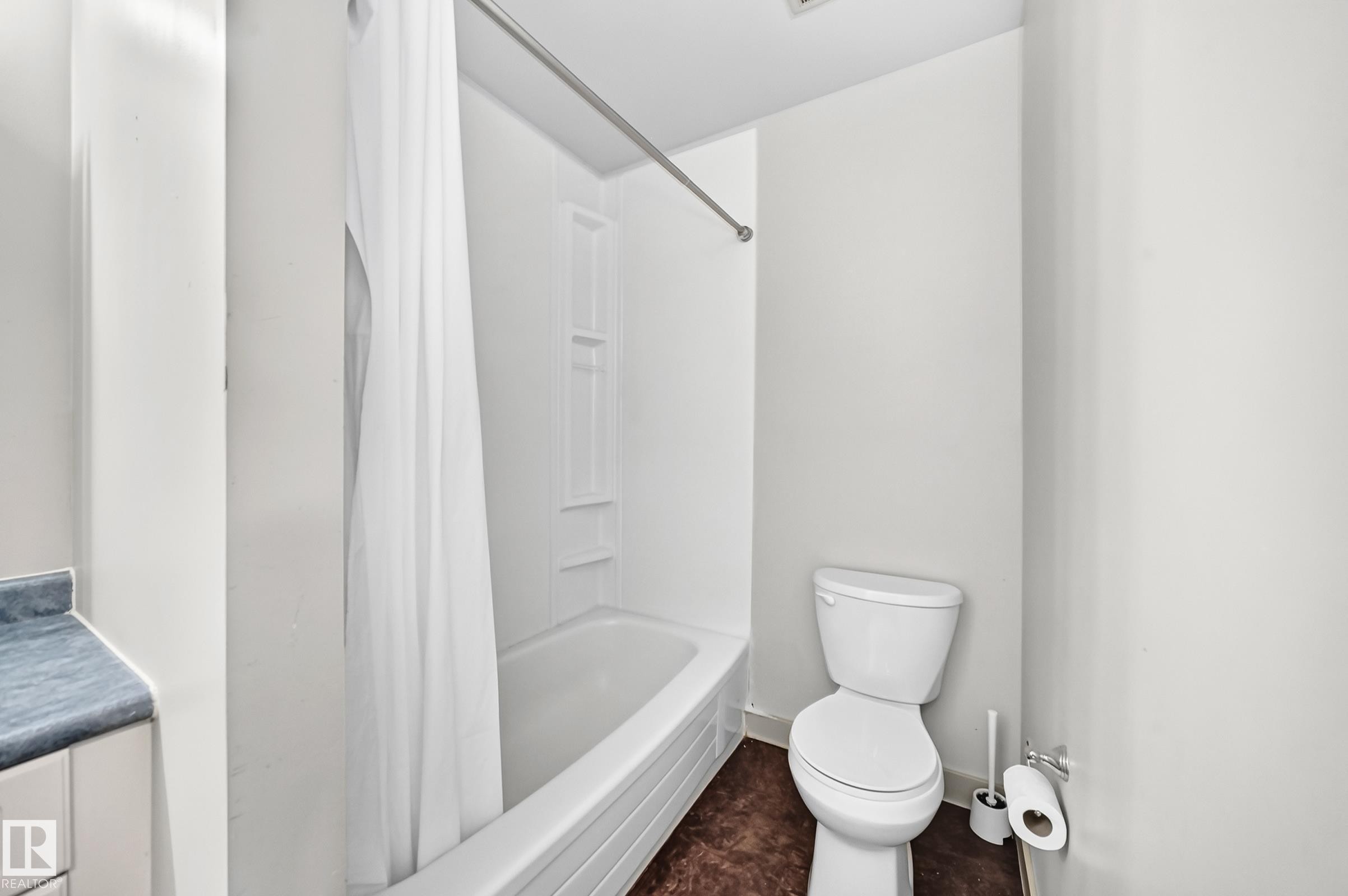 White bathtub with integrated shower, white toilet, and a built-in vanity with a blue countertop - 6416 180 Street Nw, Edmonton, AB - Indoor Photo Showing Bathroom