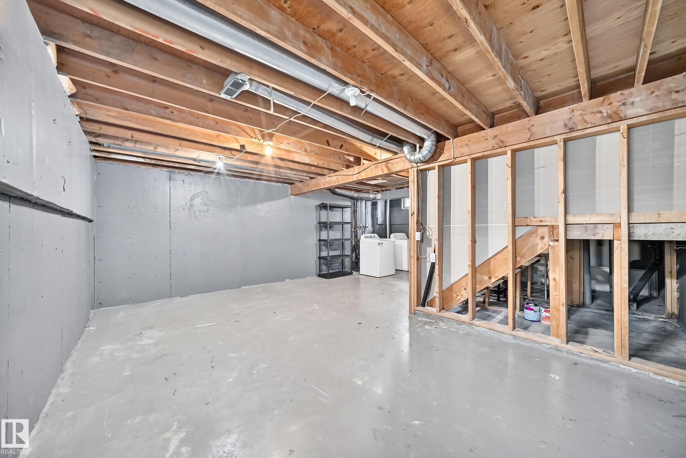 Unfinished basement with exposed wood joists, concrete flooring, and laundry appliances - 6416 180 Street Nw, Edmonton, AB - Indoor Photo Showing Basement