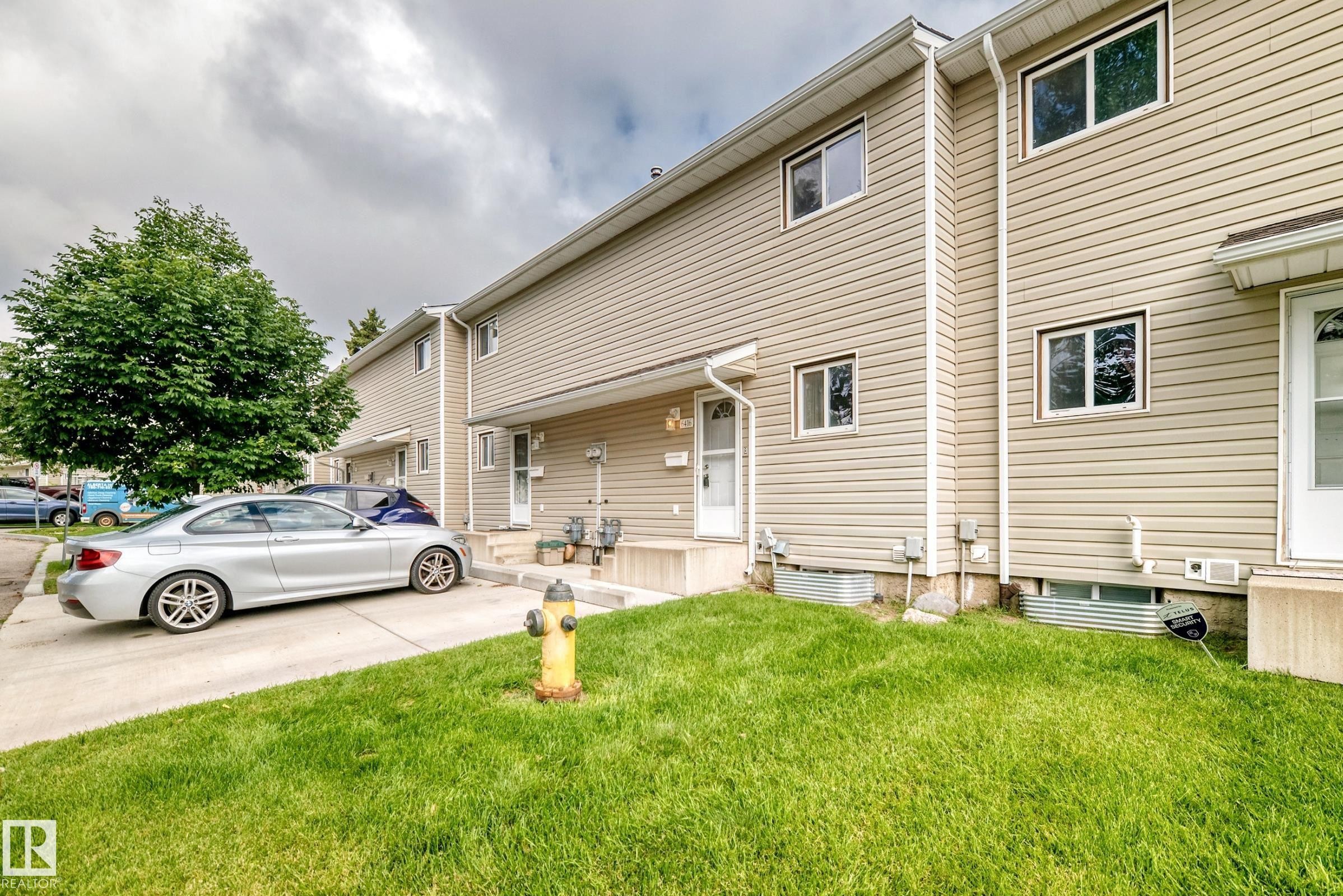 Siding exterior with multiple windows, concrete walkway, and a landscaped lawn - 6416 180 Street Nw, Edmonton, AB - Outdoor