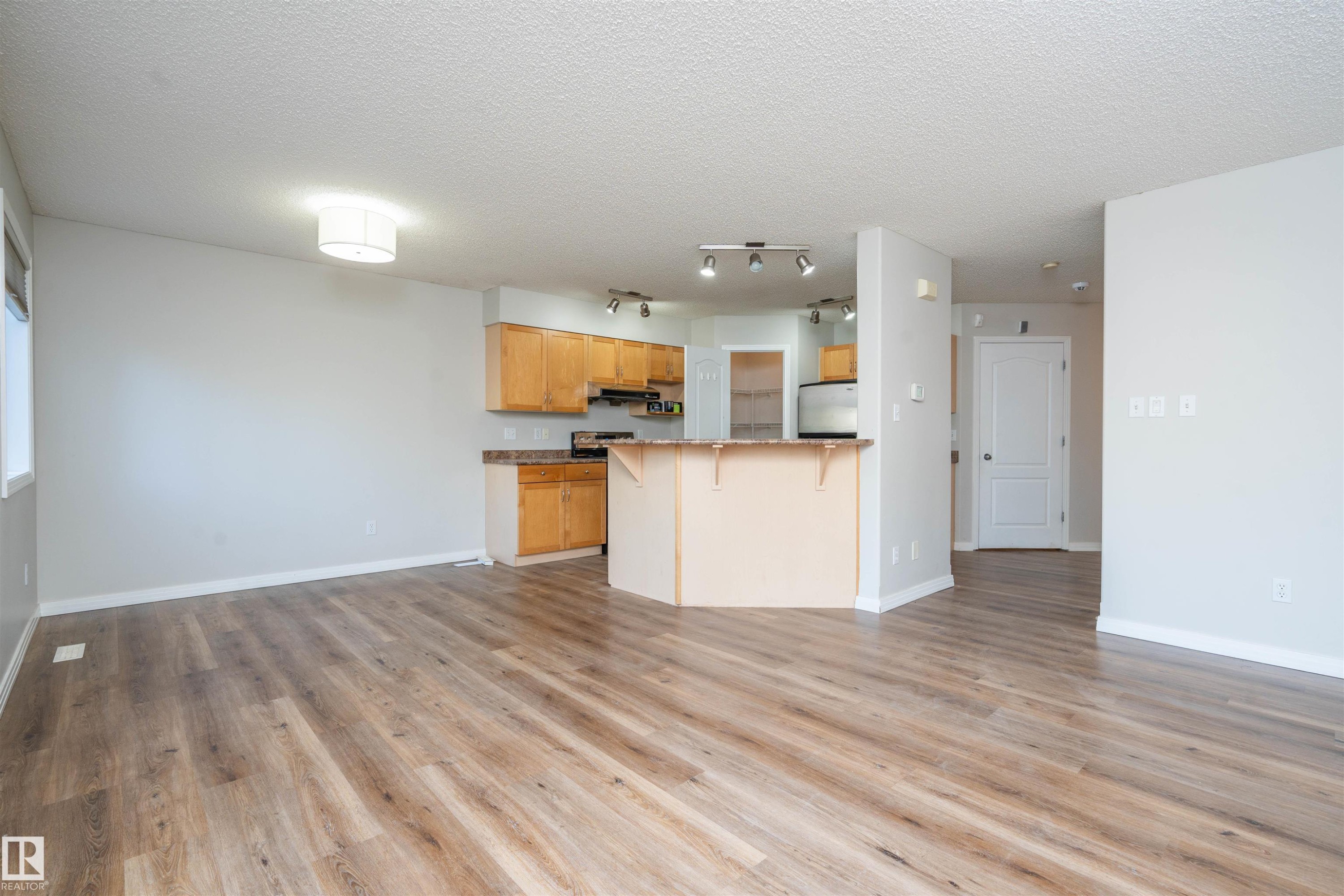 Open-concept living space featuring wood-finish flooring, a kitchen with natural wood cabinetry, stainless steel appliances, and a breakfast bar - 1009 Macewan Close Sw, Edmonton, AB - Indoor Photo Showing Kitchen