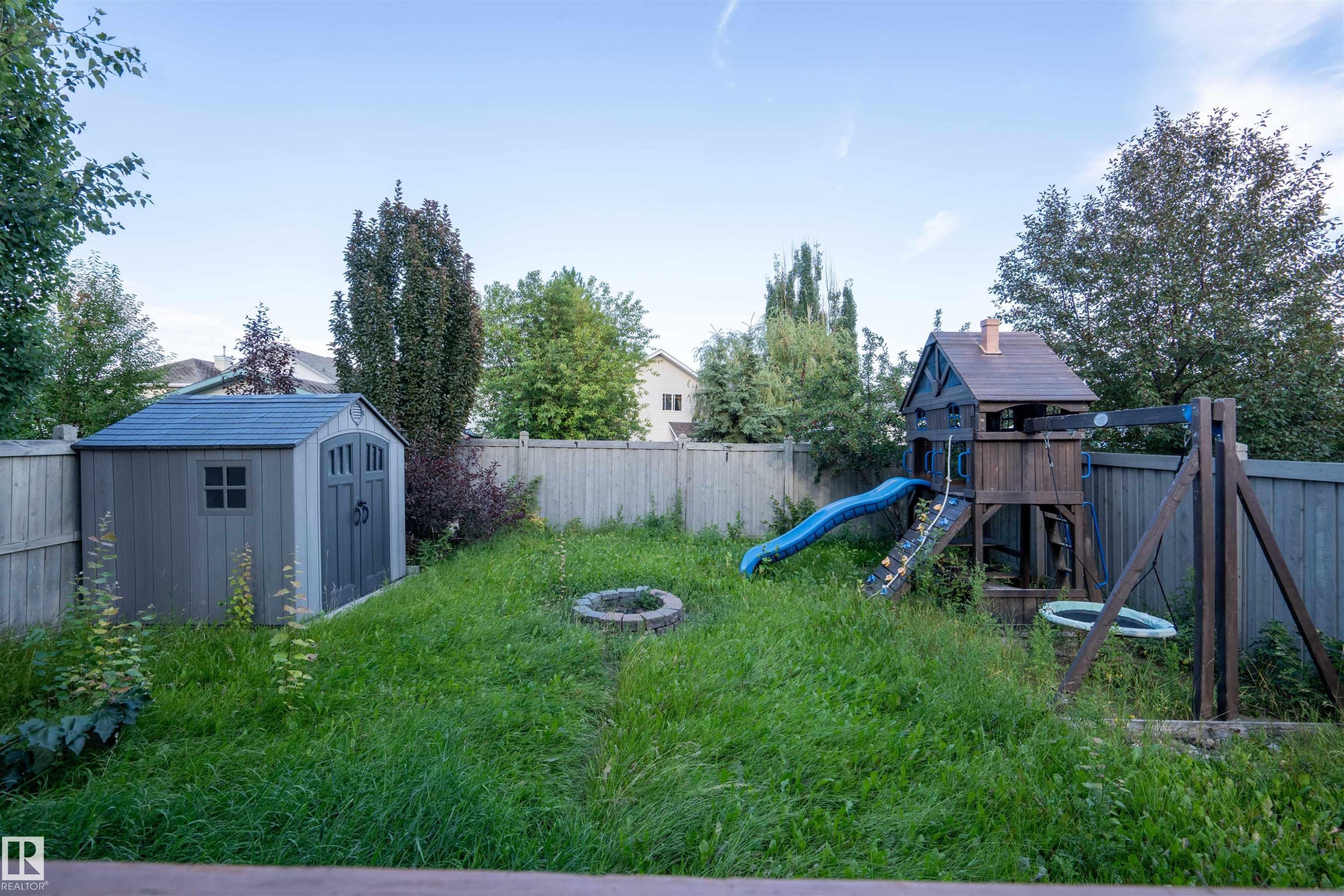 Fenced backyard featuring a storage shed, a fire pit, and mature trees - 1009 Macewan Close Sw, Edmonton, AB - Outdoor With Backyard