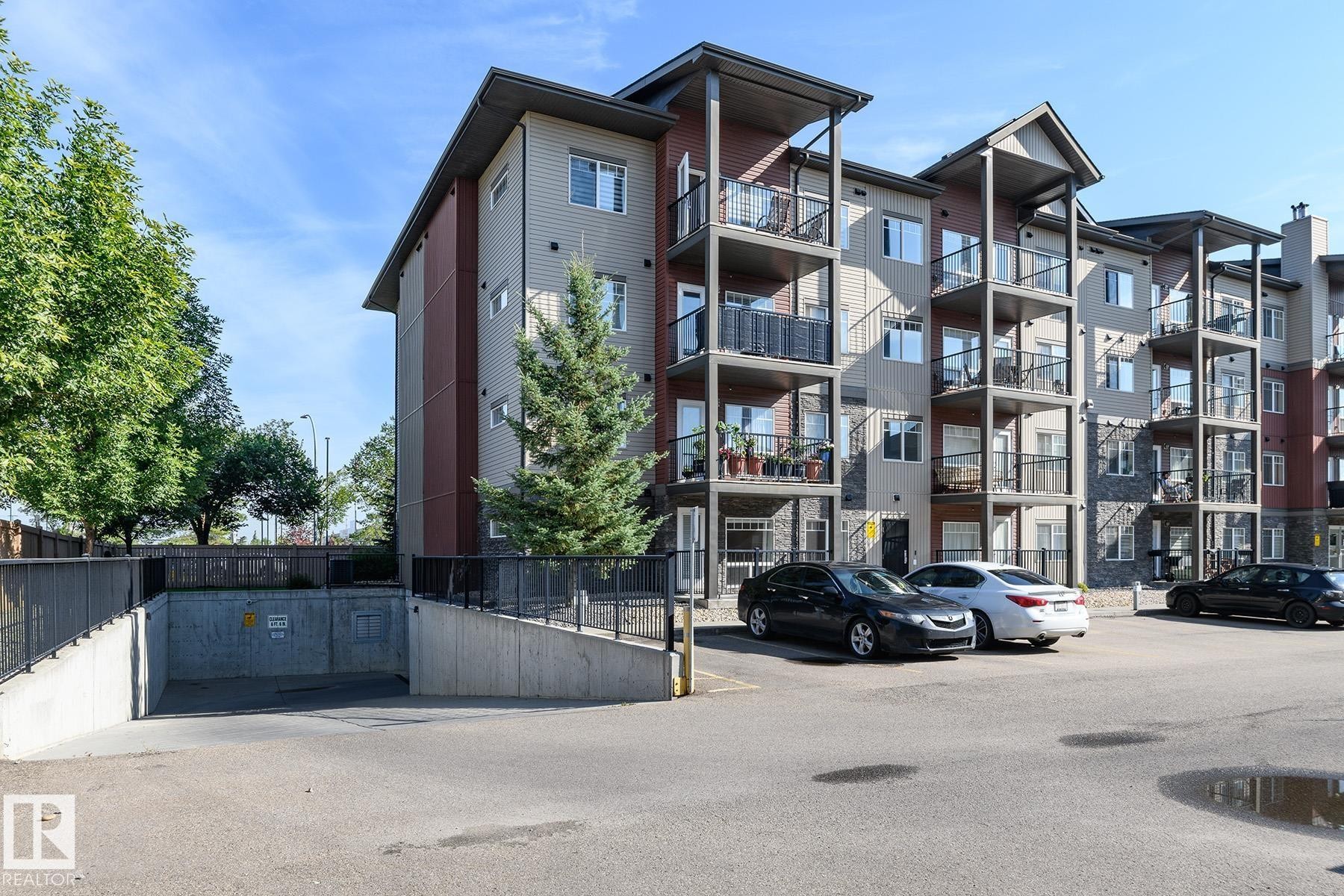 Multi-story building featuring balconies, stone accents, and a subterranean parking entrance - #110 9523 160 Av Nw, Edmonton, AB