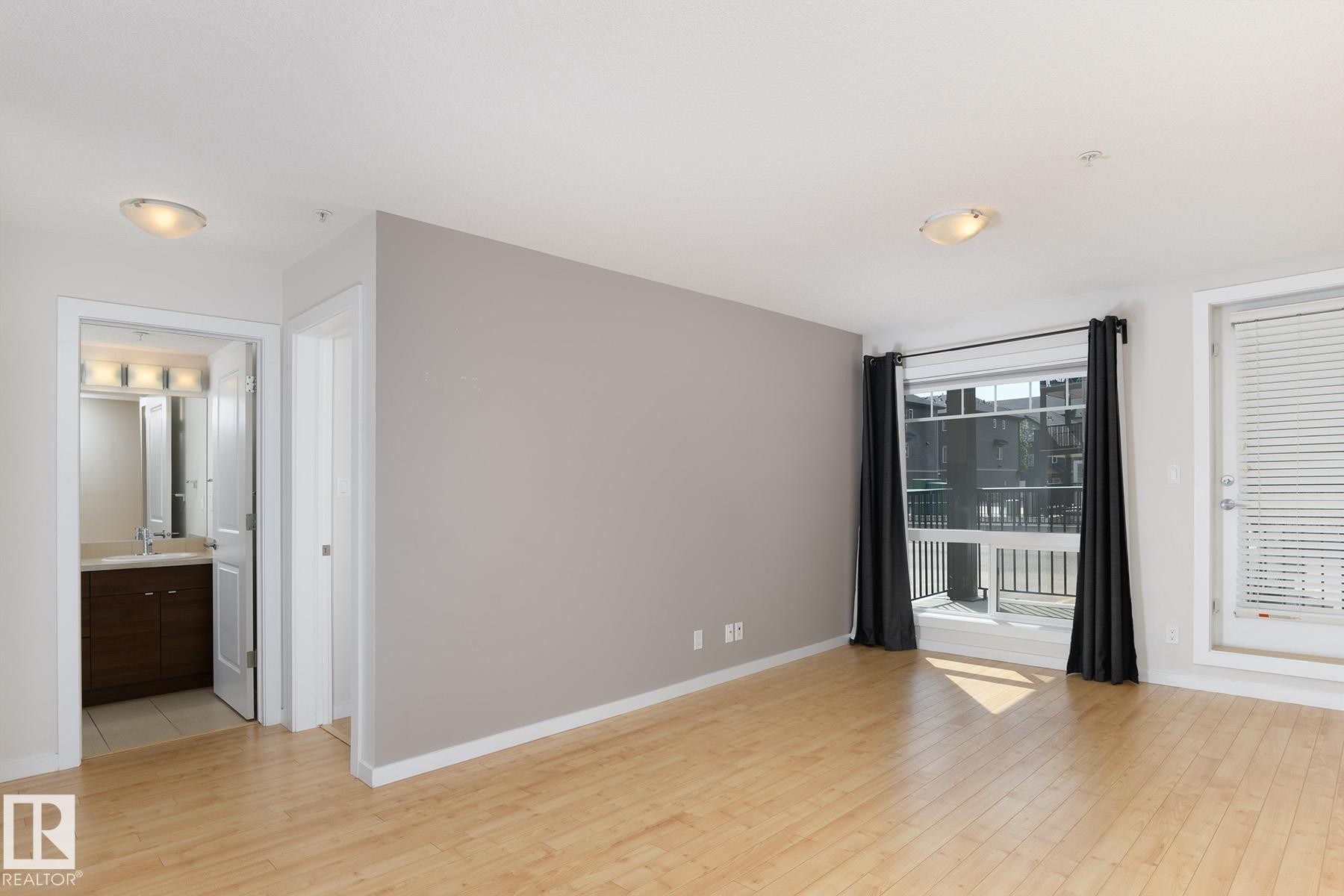 Hardwood flooring throughout, neutral paint palette, and a large window with direct balcony access - #110 9523 160 Av Nw, Edmonton, AB
