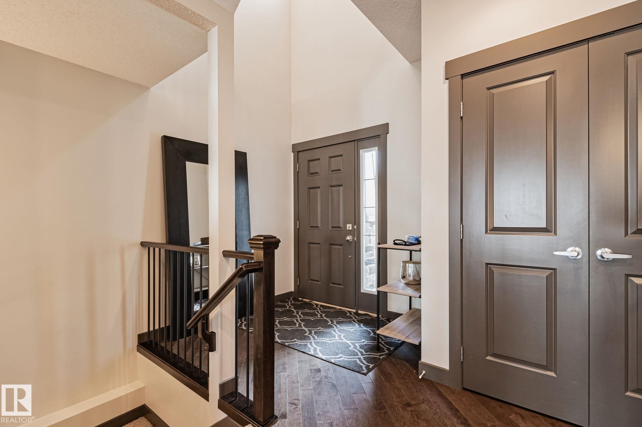 Vaulted entryway with wood-finish flooring, dark wood newel post, and paneled doors - 1337 Secord Landing Nw, Edmonton, AB - Indoor Photo Showing Other Room