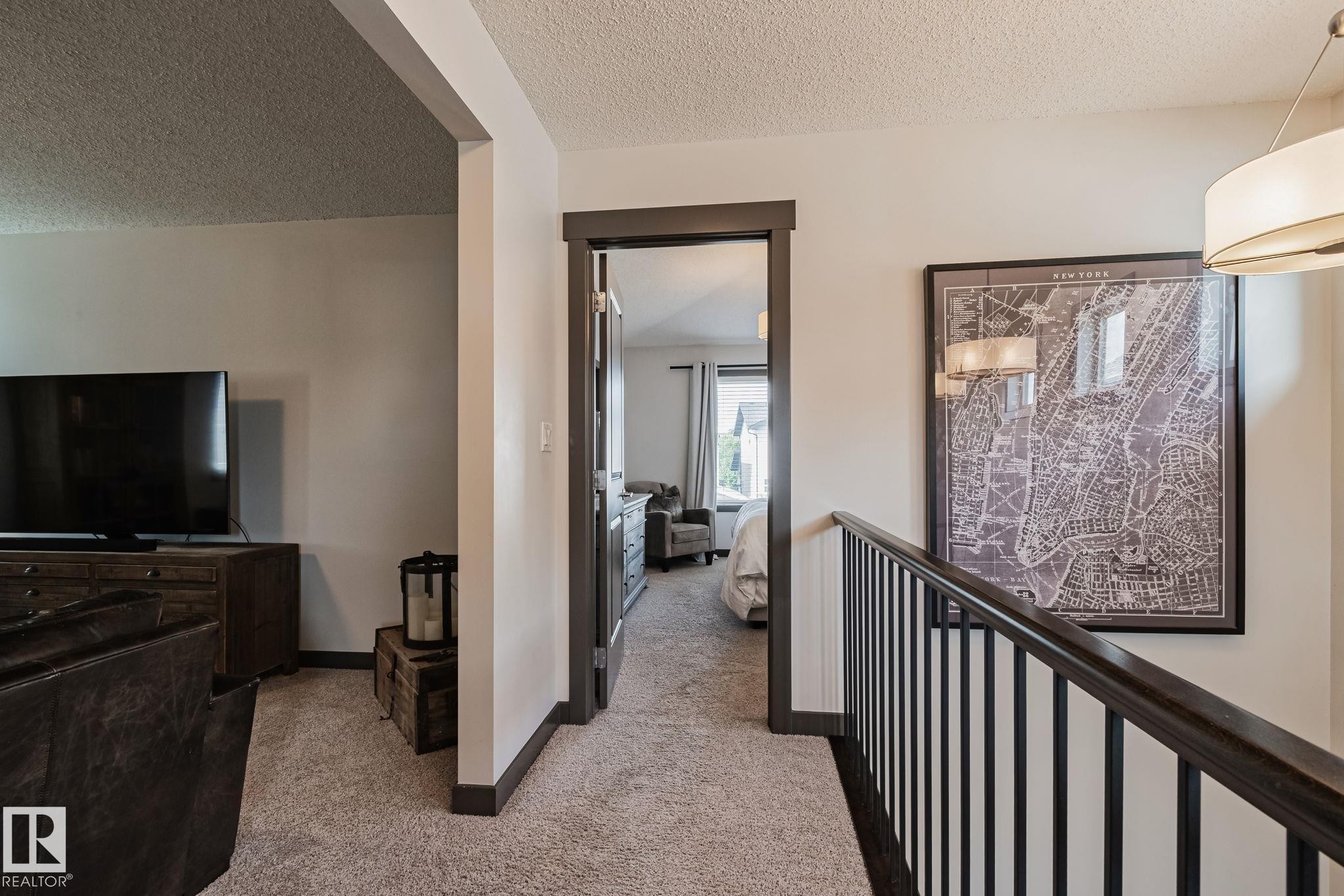Carpeted hallway with painted trim and railing, leading to a room with window - 1337 Secord Landing Nw, Edmonton, AB - Indoor Photo Showing Other Room