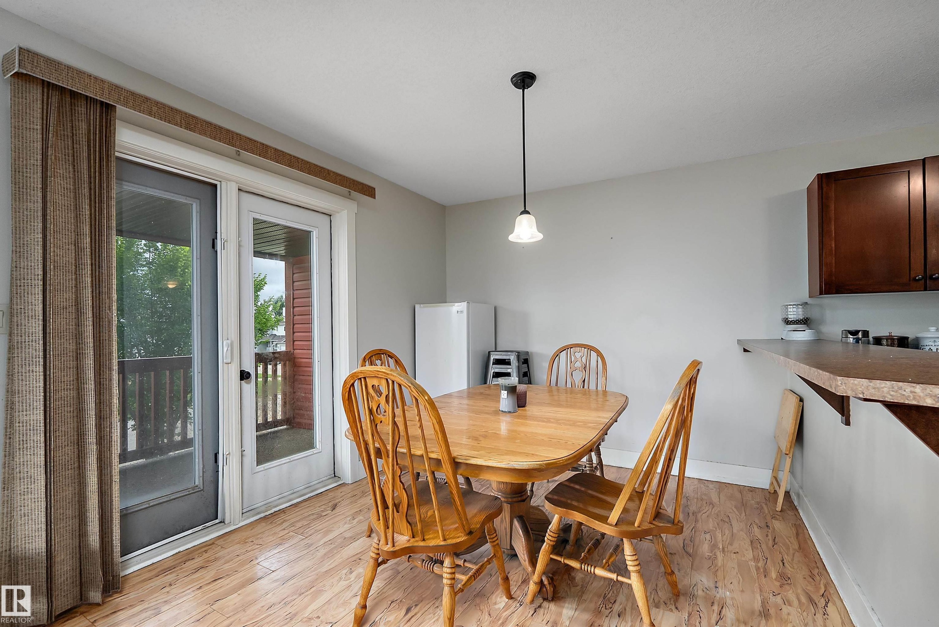 Sliding glass door leading to a balcony, wood-finish flooring, and a breakfast bar with built-in cabinetry - 203 Graybriar Green, Stony Plain, AB - Indoor Photo Showing Dining Room