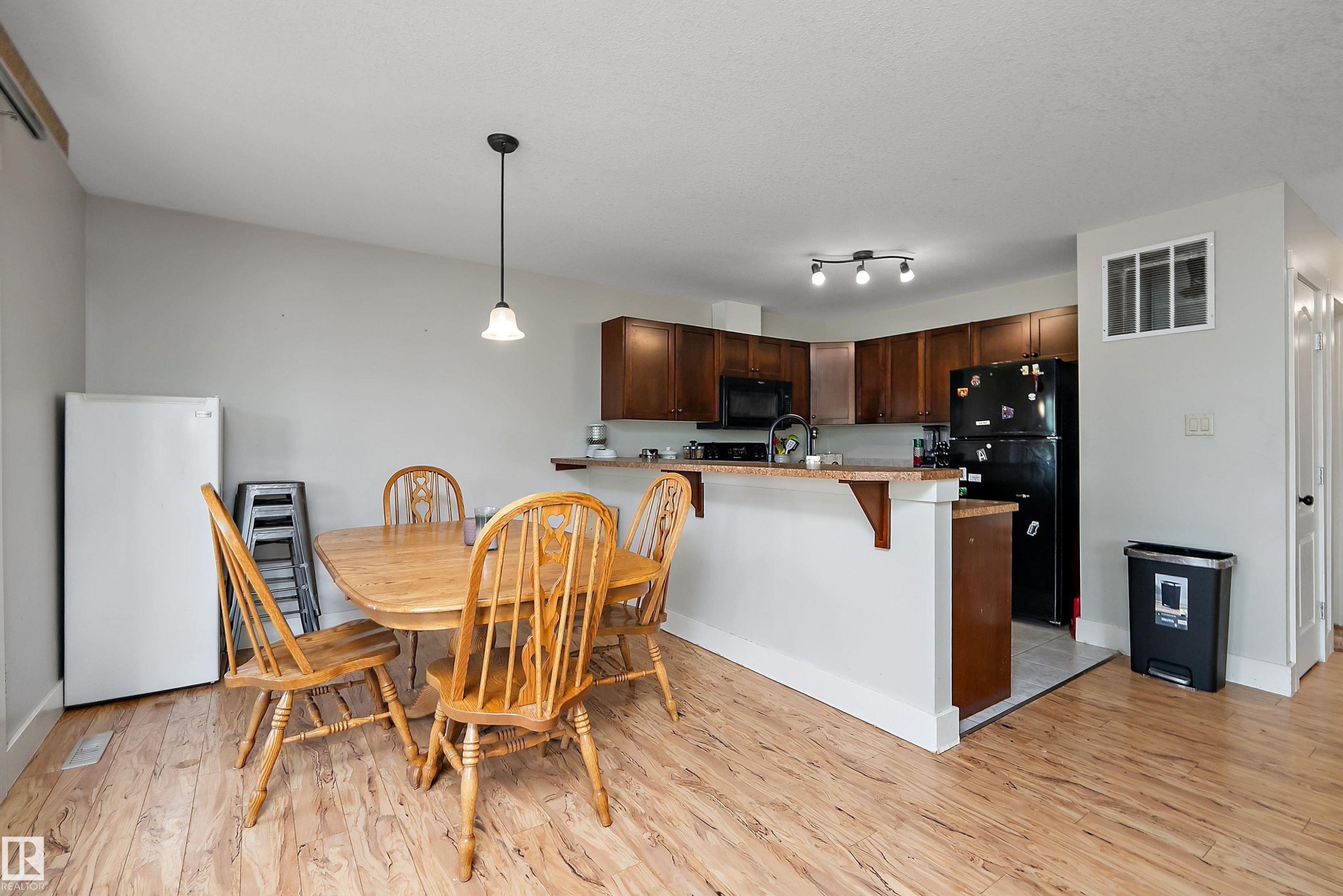 Open-concept kitchen and dining area featuring wood-finish flooring, dark wood cabinetry, a breakfast bar, and track lighting - 203 Graybriar Green, Stony Plain, AB - Indoor