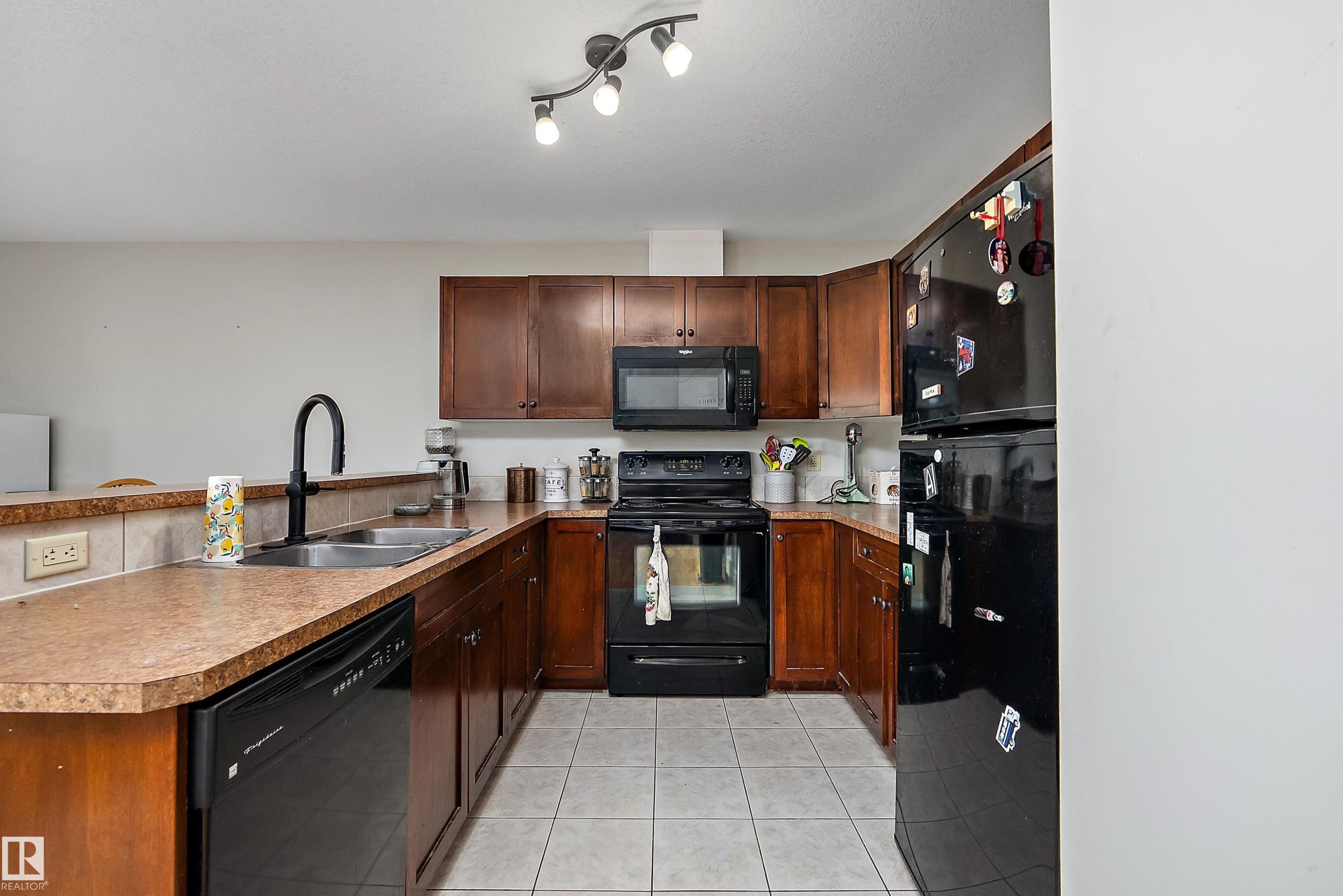 U-shaped kitchen featuring wood cabinetry, stone-finish countertops, tile backsplash, and tile flooring - 203 Graybriar Green, Stony Plain, AB - Indoor Photo Showing Kitchen With Double Sink