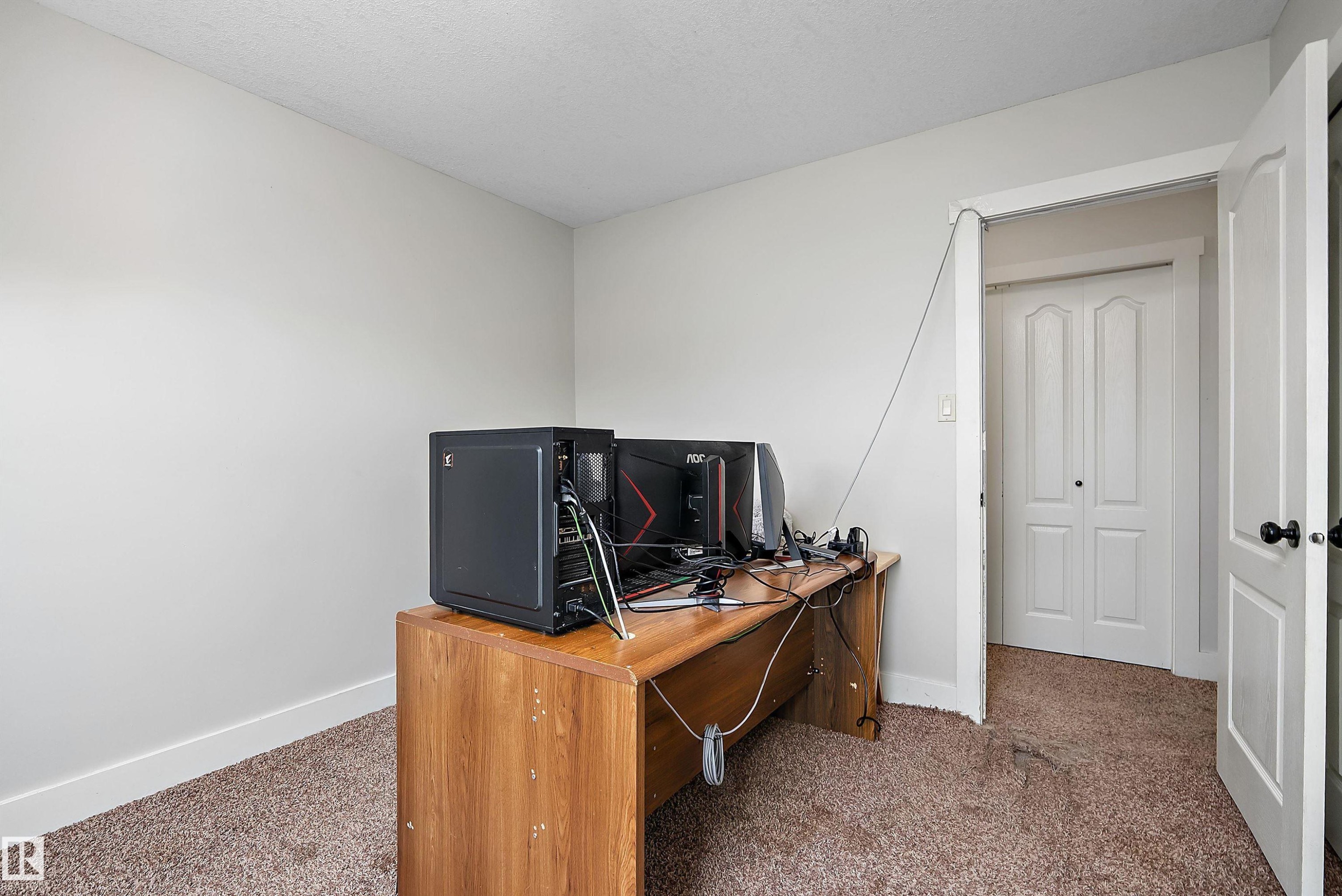 Textured carpet flooring, neutral wall paint, white trim, and white bi-fold closet doors - 203 Graybriar Green, Stony Plain, AB - Indoor Photo Showing Office