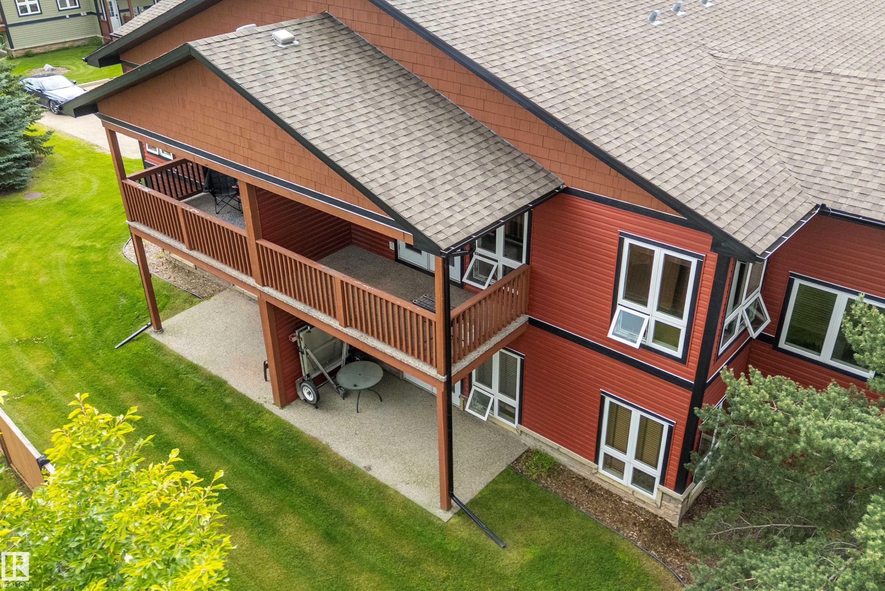 Red exterior siding with white-framed windows, a multi-level deck, ground-level patio, and shingle roofing - 203 Graybriar Green, Stony Plain, AB - Outdoor With Deck Patio Veranda With Exterior