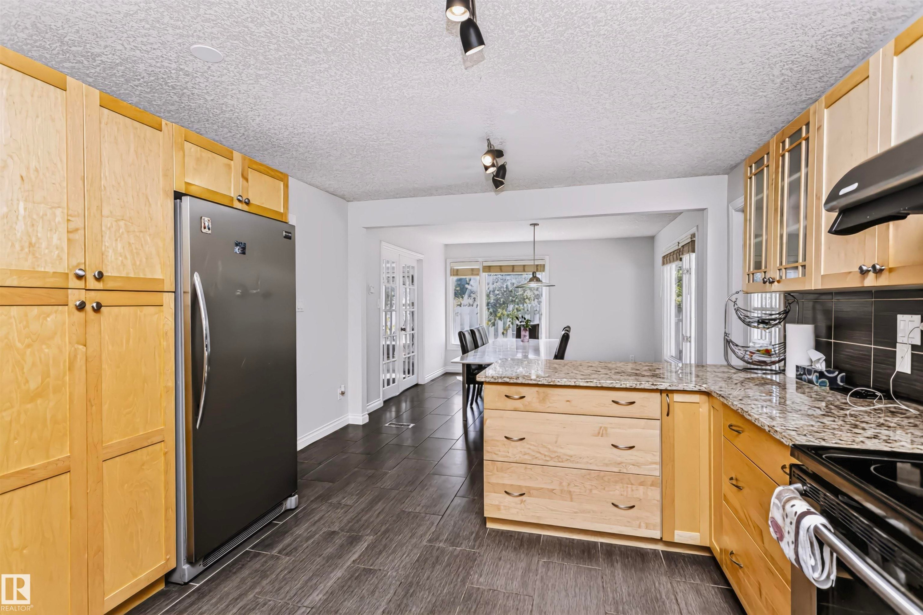 Kitchen featuring wood-finish cabinetry, granite countertops, tile flooring, and a stainless steel refrigerator - 6016 177 Street Nw, Edmonton, AB - Indoor Photo Showing Kitchen