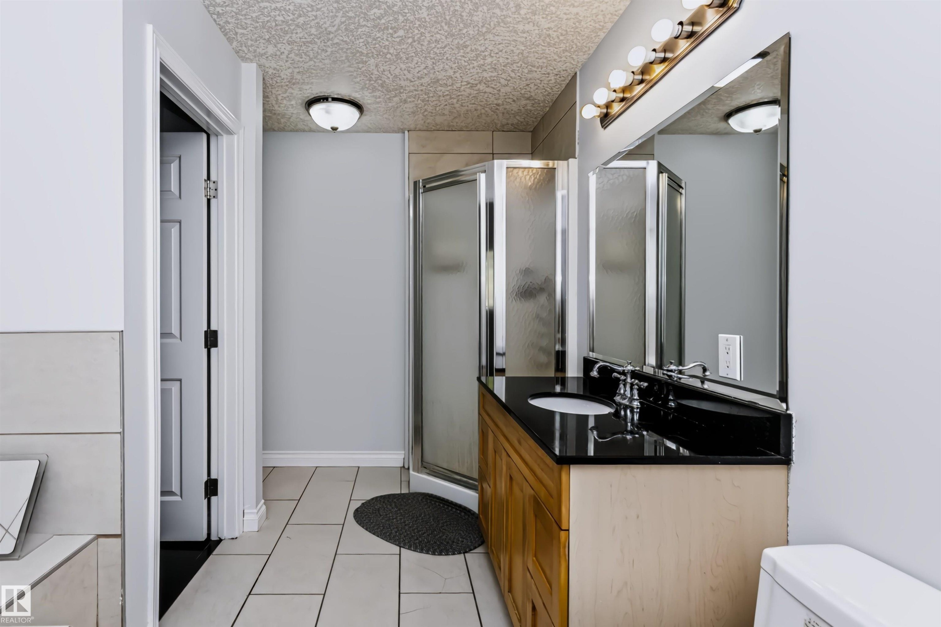 Vanity with dark countertop, large mirror, and overhead lighting - 6016 177 Street Nw, Edmonton, AB - Indoor Photo Showing Bathroom