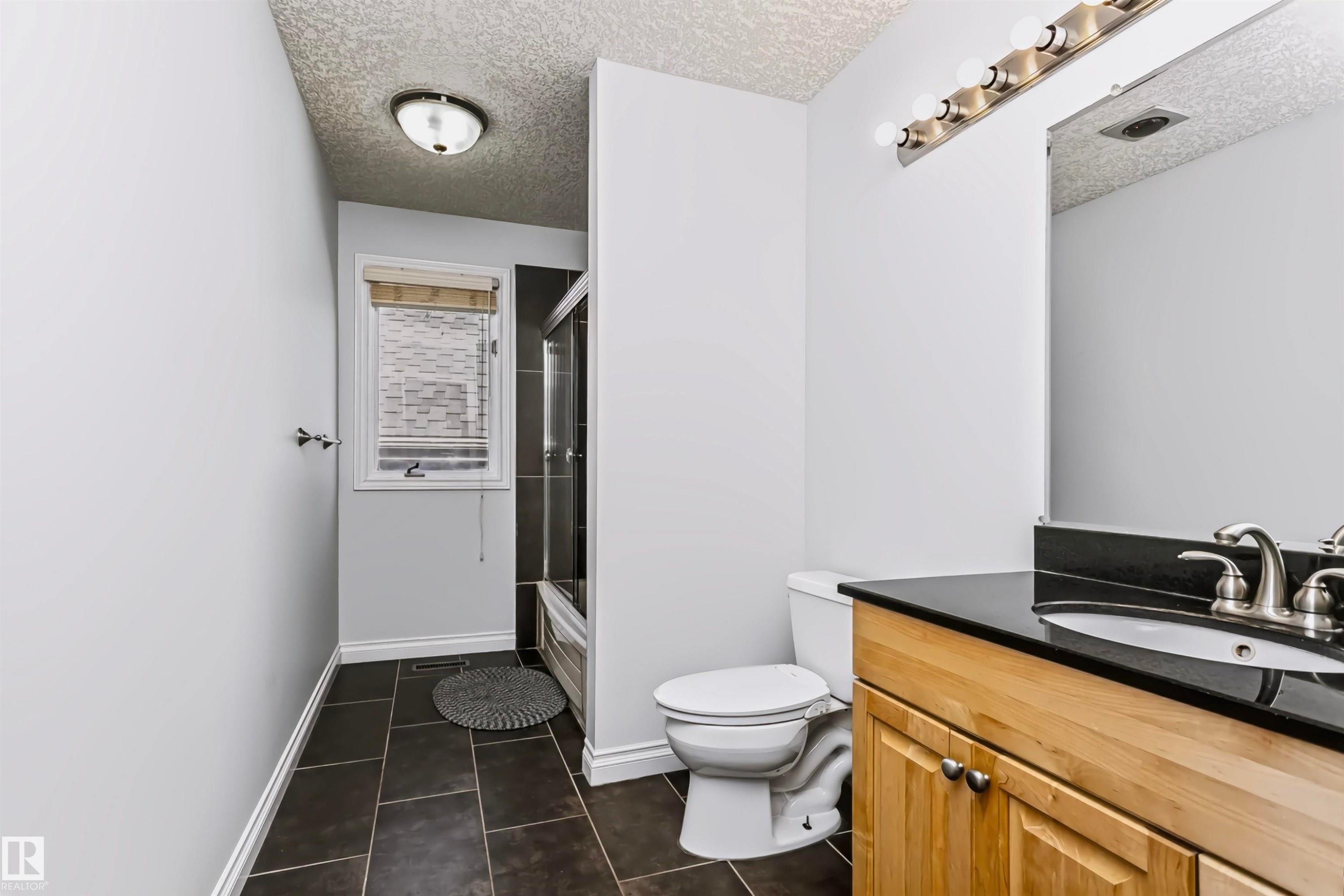 Bathroom featuring a wood-finish vanity with a dark countertop, an integrated sink, and a framed mirror - 6016 177 Street Nw, Edmonton, AB - Indoor Photo Showing Bathroom