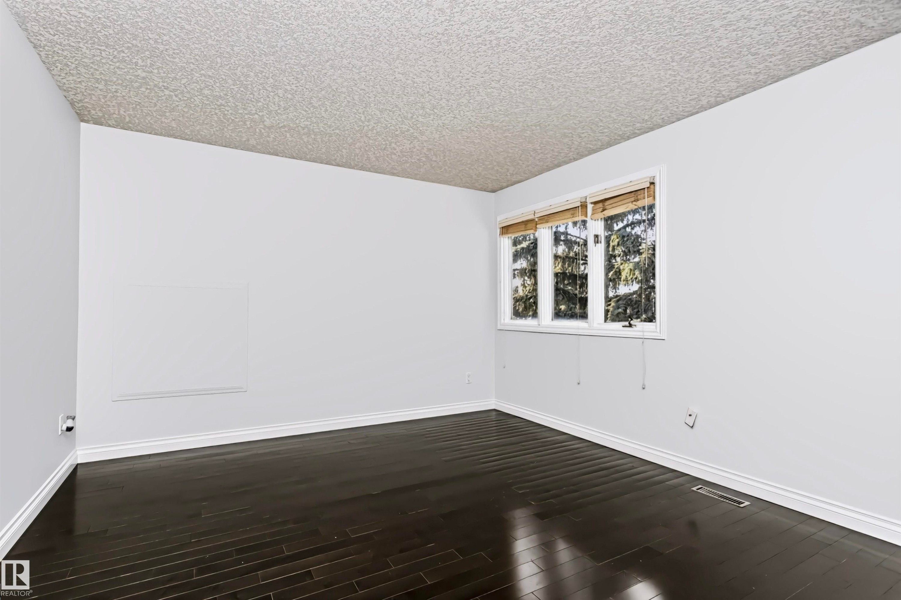 Dark wood-finish flooring with white baseboards, a white wall finish, and a textured ceiling - 6016 177 Street Nw, Edmonton, AB - Indoor Photo Showing Other Room