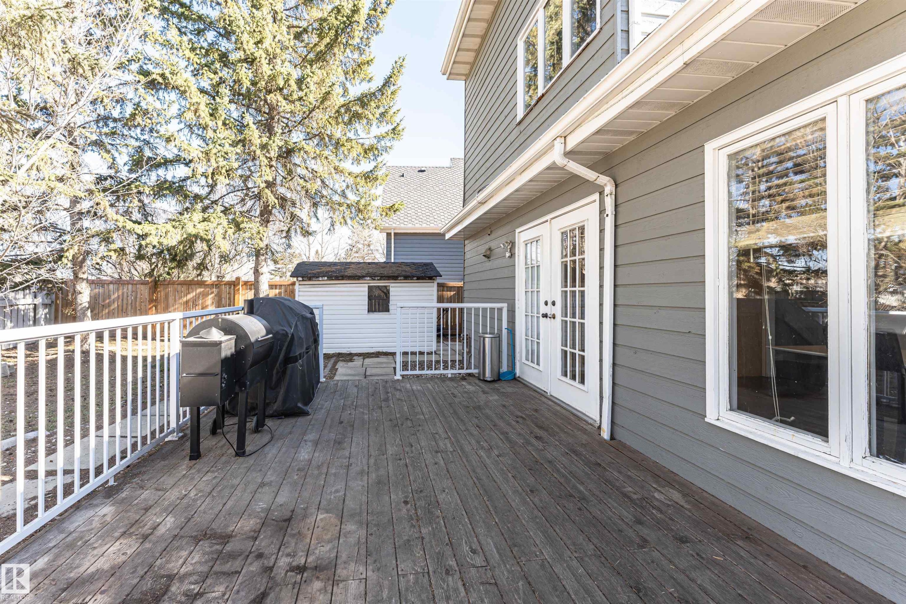 Expansive wood deck with white railing, featuring double French doors and a storage shed within the fenced yard - 6016 177 Street Nw, Edmonton, AB - Outdoor With Deck Patio Veranda With Exterior