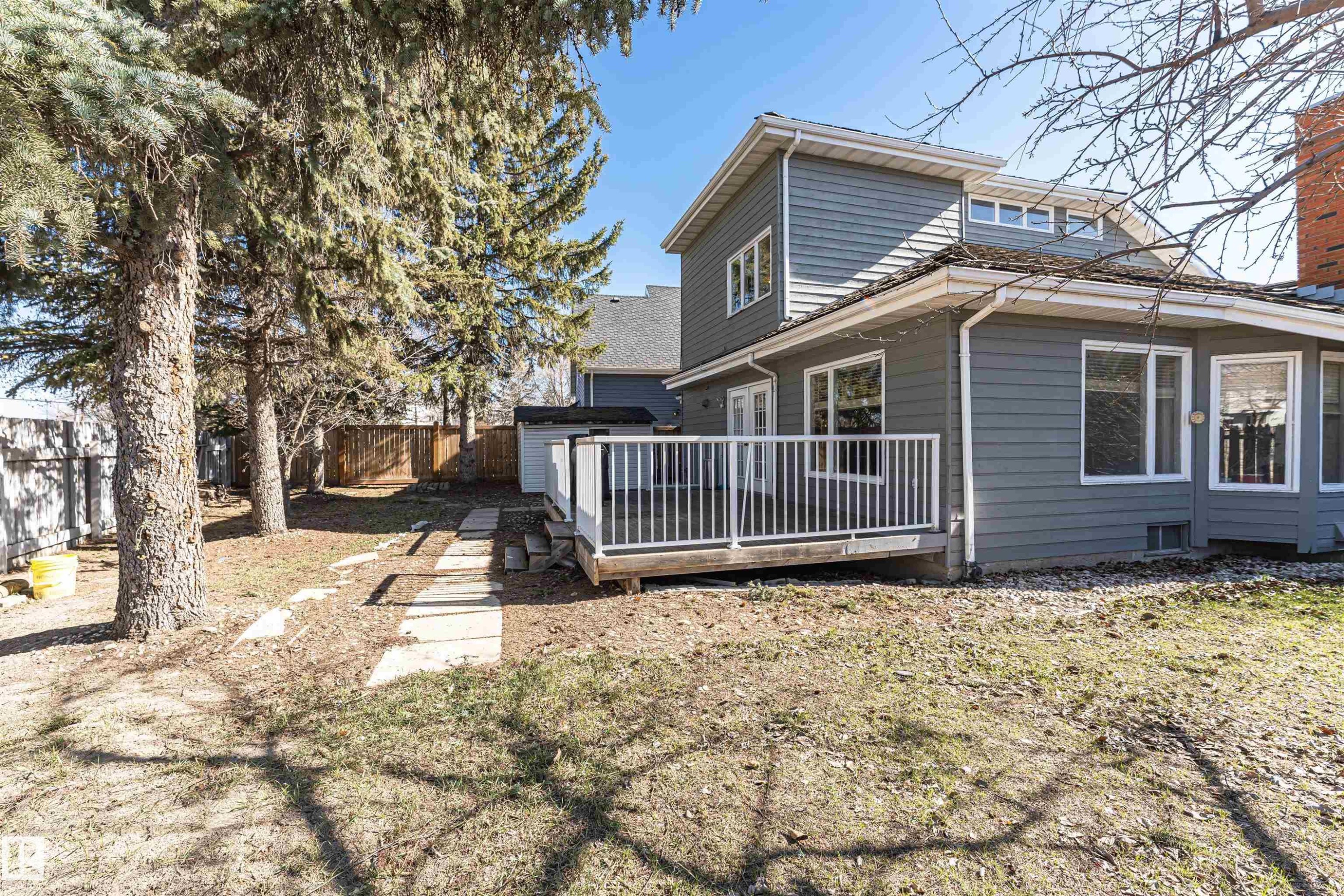 Rear exterior featuring gray siding, a wood deck with white railings, multiple windows, and a storage shed - 6016 177 Street Nw, Edmonton, AB - Outdoor
