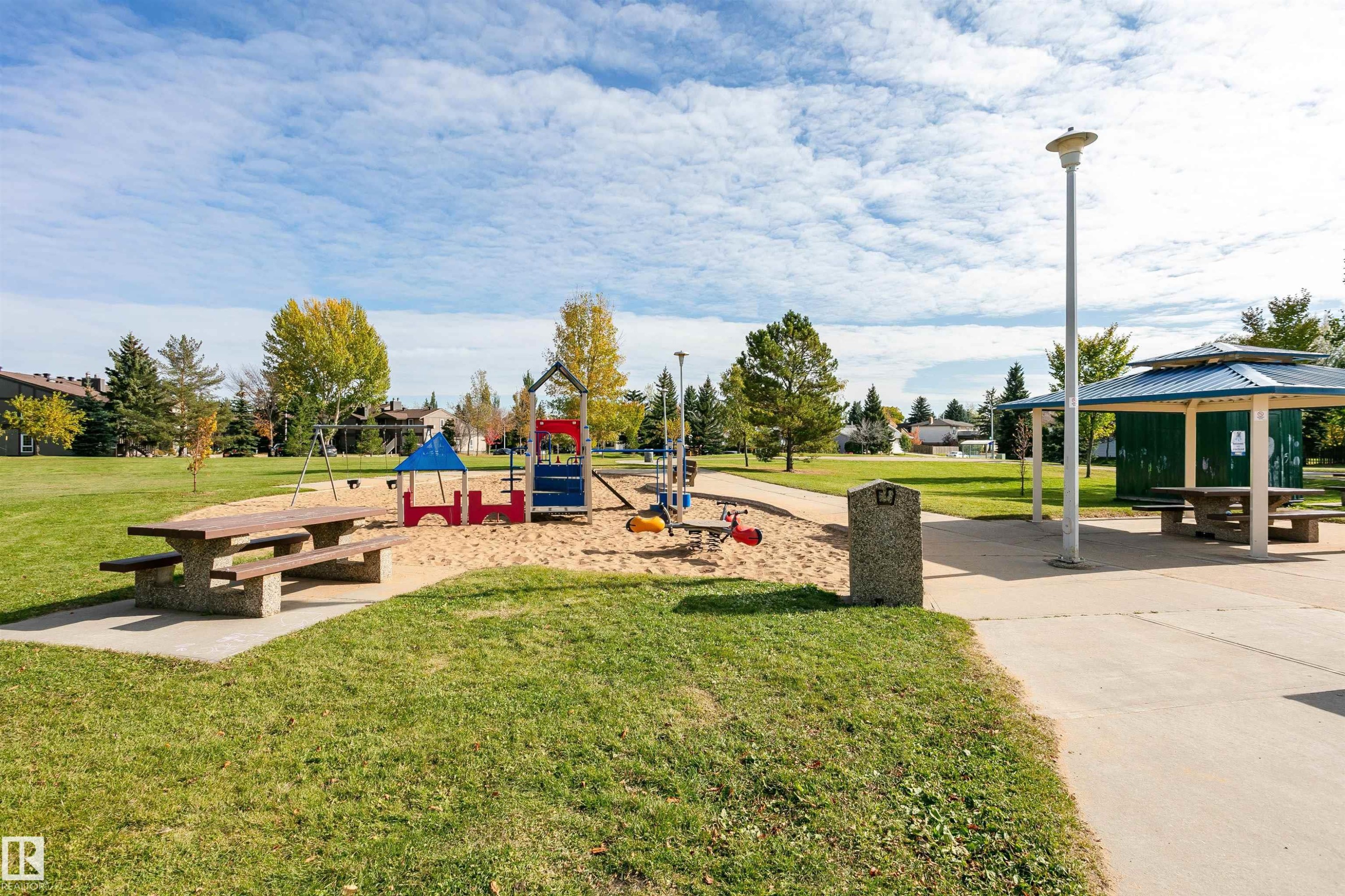 Expansive green space featuring a playground with sand, concrete picnic tables, mature trees, and a covered picnic area - 6016 177 Street Nw, Edmonton, AB - Outdoor