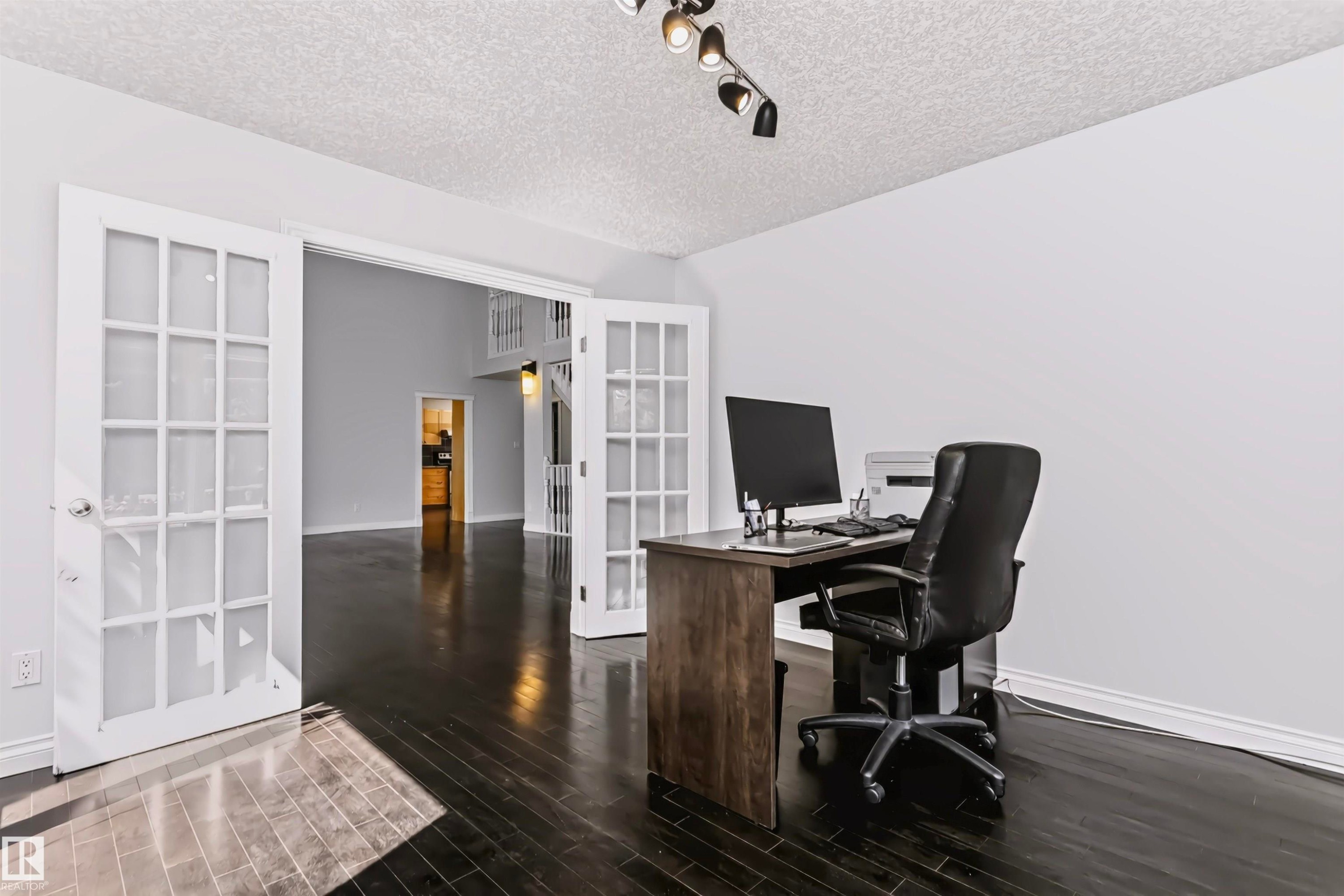 Double French doors with glass panes, dark wood-finish flooring, white walls, and track lighting - 6016 177 Street Nw, Edmonton, AB - Indoor Photo Showing Office