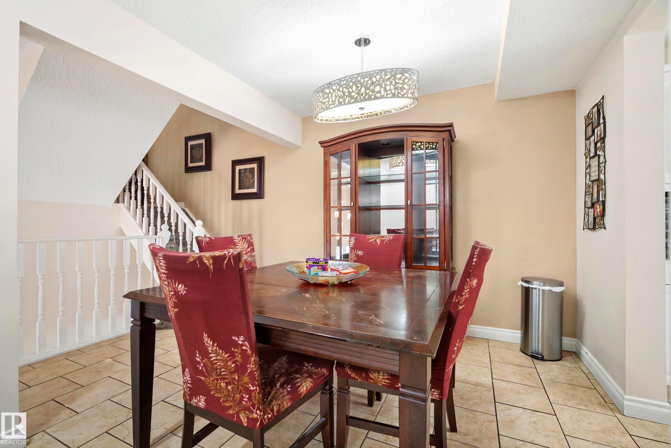 Dining area featuring large format tile flooring, a decorative chandelier, and a wood staircase with white balusters - #25 3811 85 St Nw, Edmonton, AB - Indoor Photo Showing Dining Room