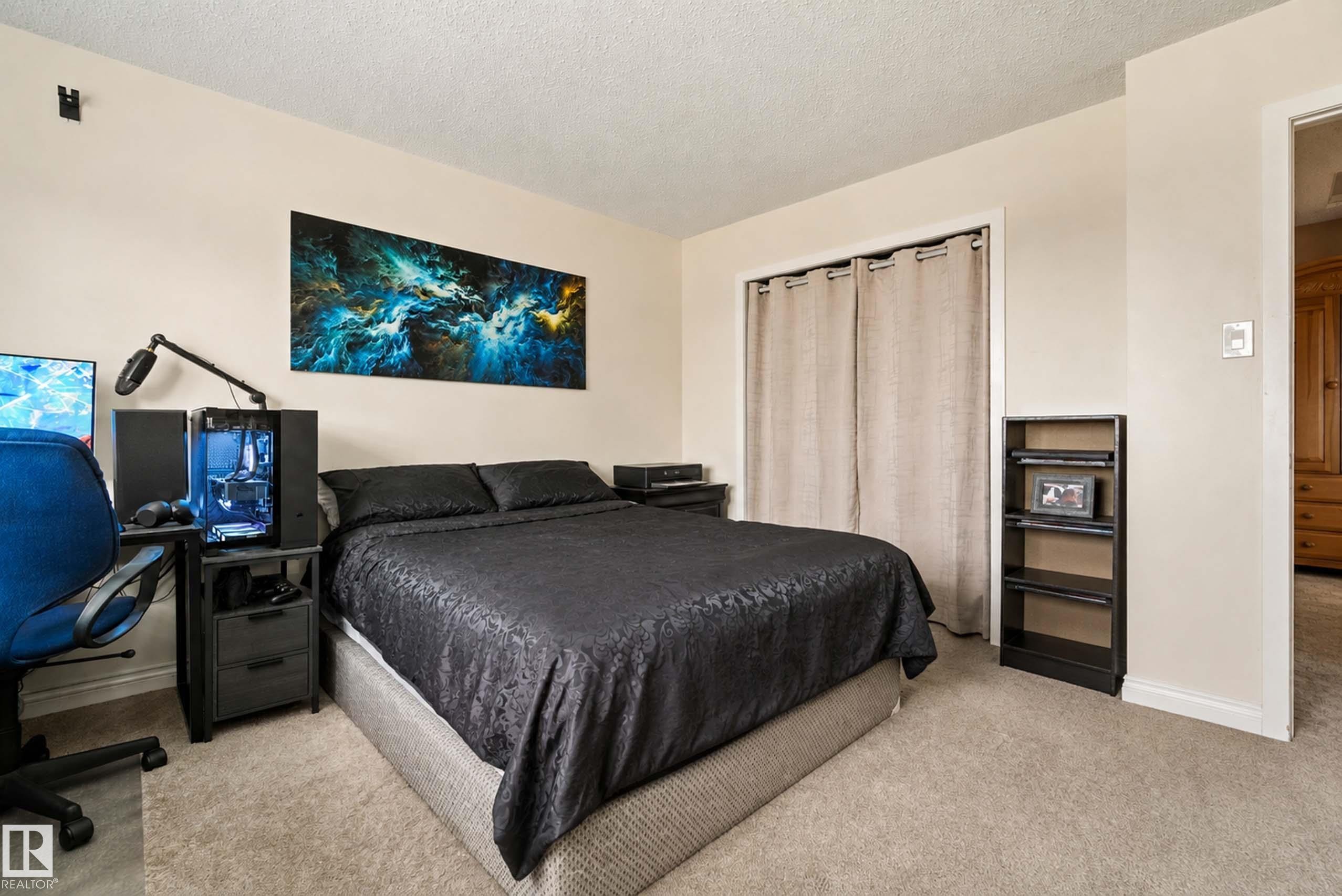 Spacious bedroom with neutral carpeting, black upholstered bed frame, and soft ambient lighting - #25 3811 85 St Nw, Edmonton, AB - Indoor Photo Showing Bedroom