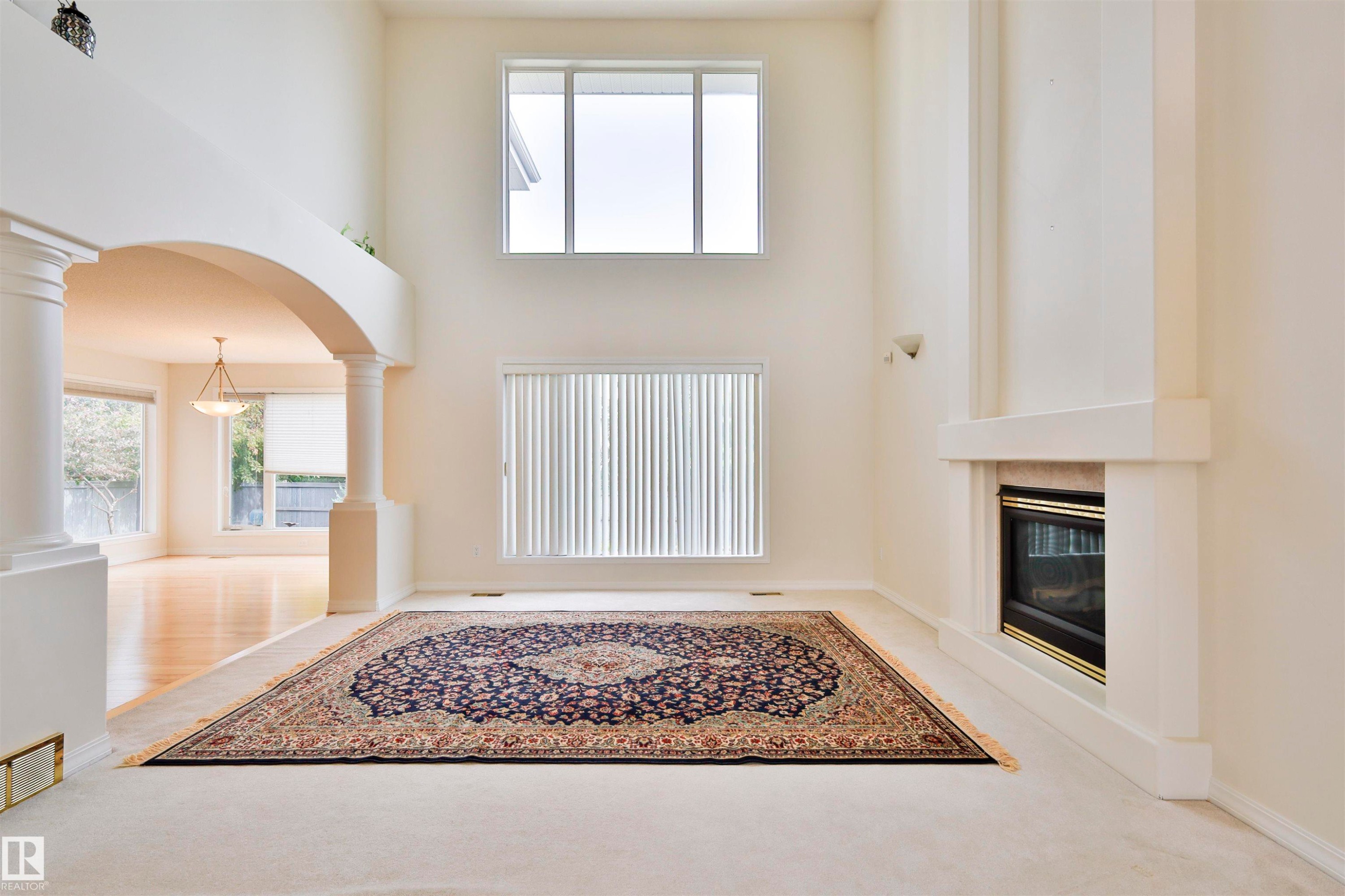Vaulted ceiling, arched entryway with decorative columns, integrated fireplace with a stone surround, and hardwood flooring in the adjacent space - 237 Darlington Crescent Nw, Edmonton, AB - Indoor Photo Showing Other Room With Fireplace