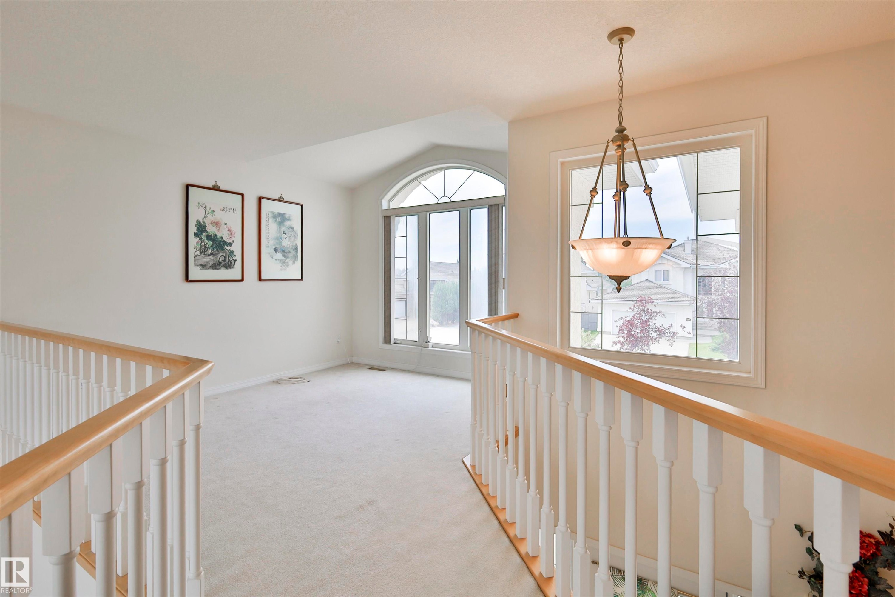 Arched window, second window with decorative muntins, neutral carpet, white wall color, and wood handrails - 237 Darlington Crescent Nw, Edmonton, AB - Indoor Photo Showing Other Room