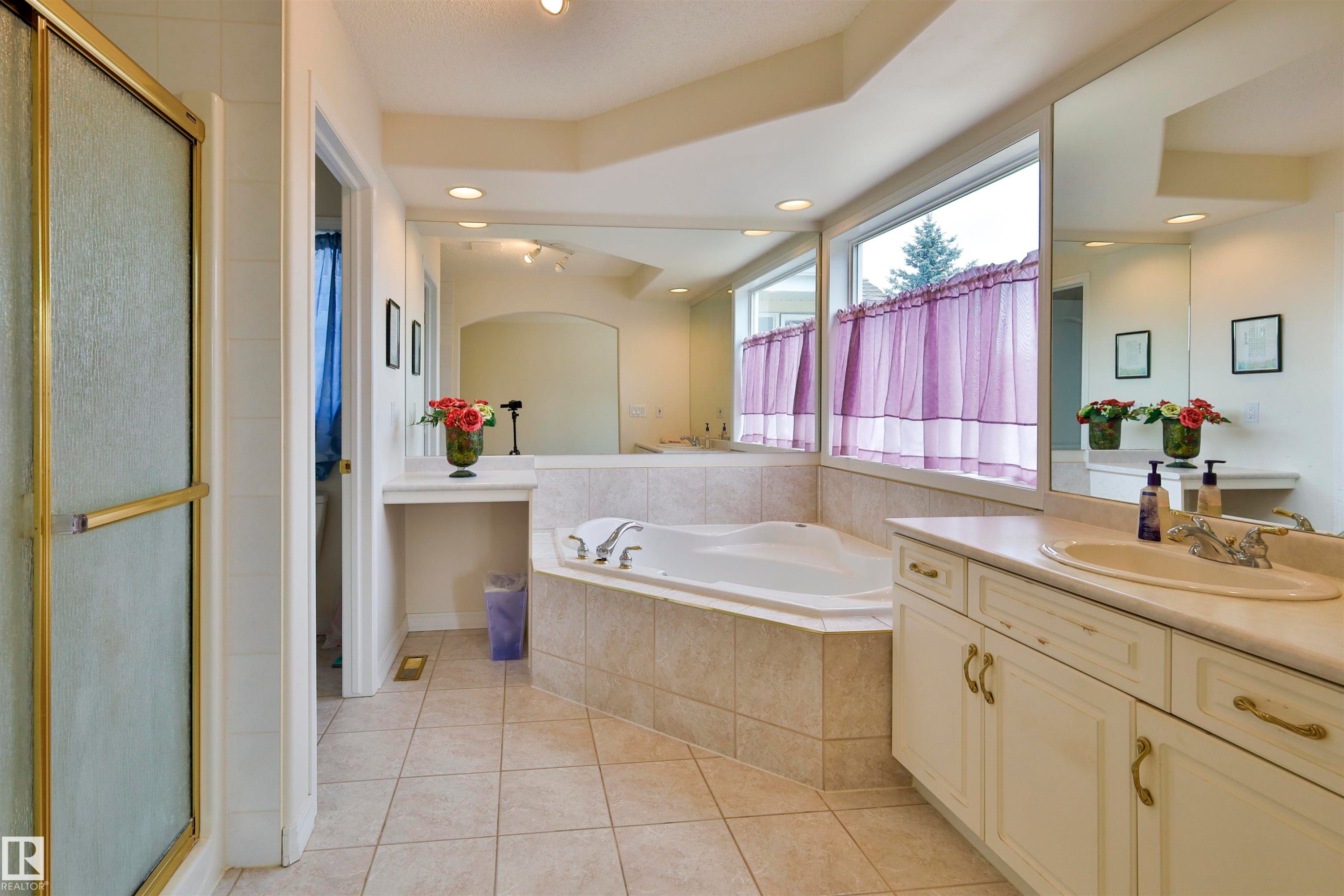 Tile flooring with a corner soaking tub, a single vanity with an integrated sink, and an enclosed shower with a gold-finish frame - 237 Darlington Crescent Nw, Edmonton, AB - Indoor Photo Showing Bathroom