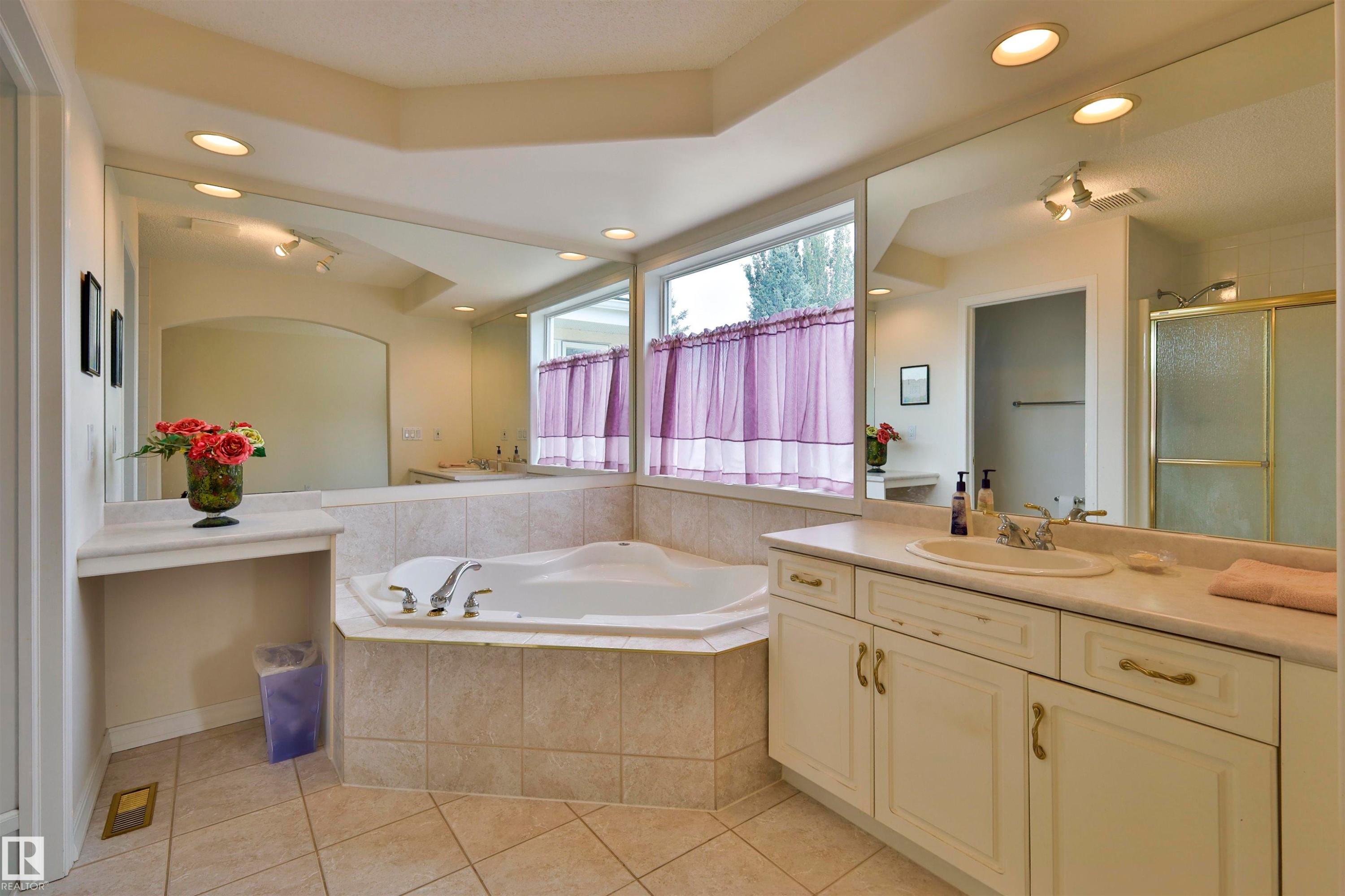 Recessed lighting illuminates a built-in corner soaking tub with tile surround, a spacious vanity with an integrated sink, and an expansive wall-mounted mirror - 237 Darlington Crescent Nw, Edmonton, AB - Indoor Photo Showing Bathroom