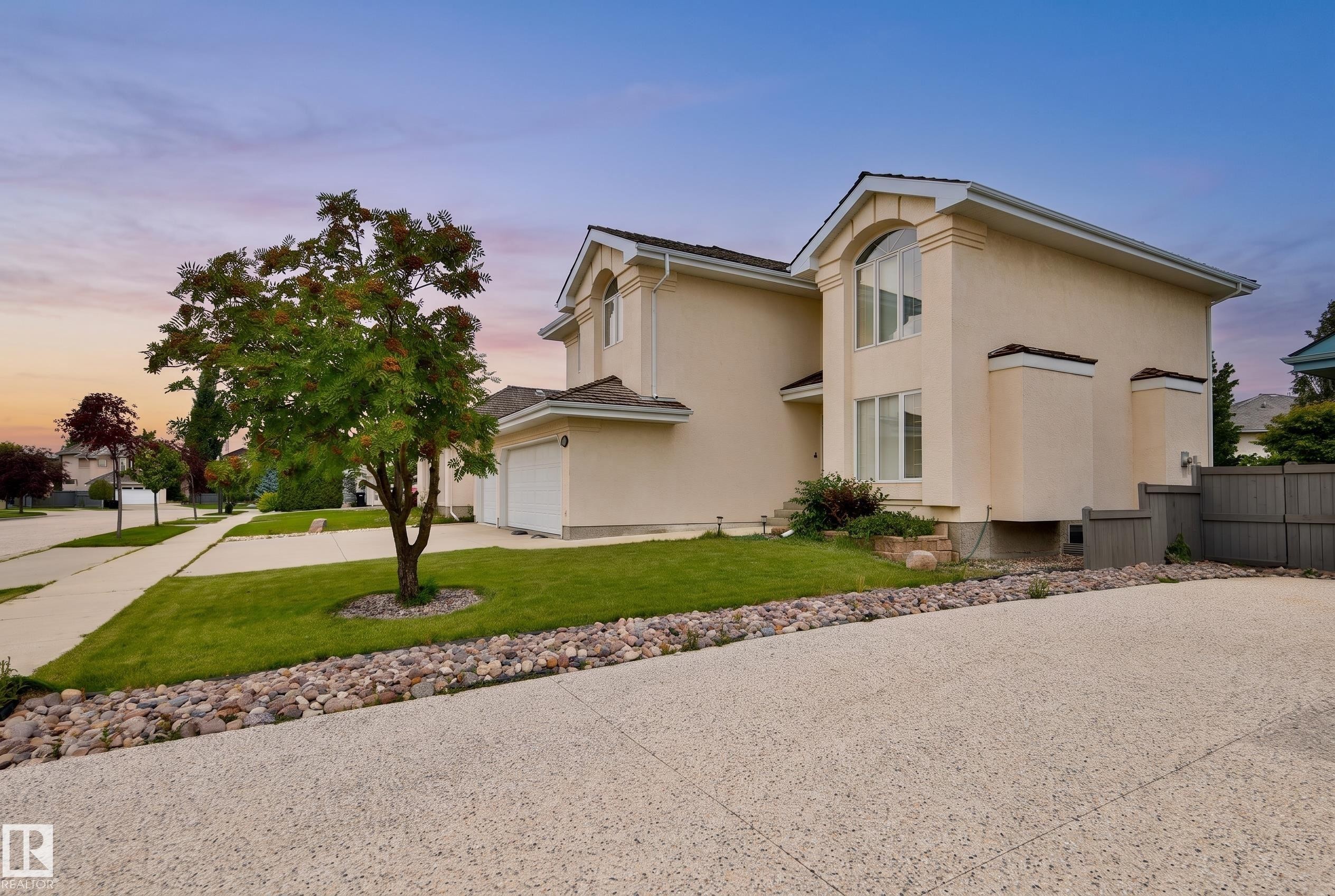 Stucco exterior with an arched window, attached garage, concrete driveway, and a manicured lawn with decorative rock landscaping - 237 Darlington Crescent Nw, Edmonton, AB - Outdoor