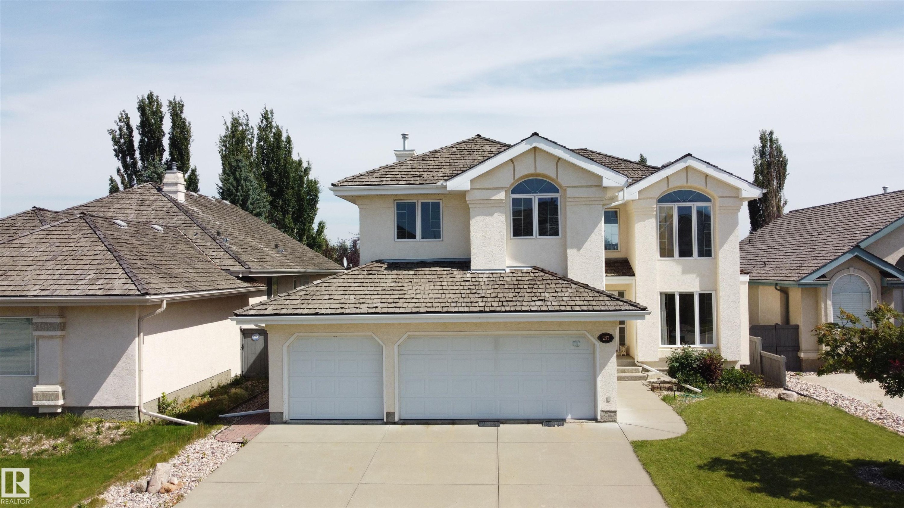 Stucco exterior featuring dual arched windows and a two-car garage - 237 Darlington Crescent Nw, Edmonton, AB - Outdoor With Facade