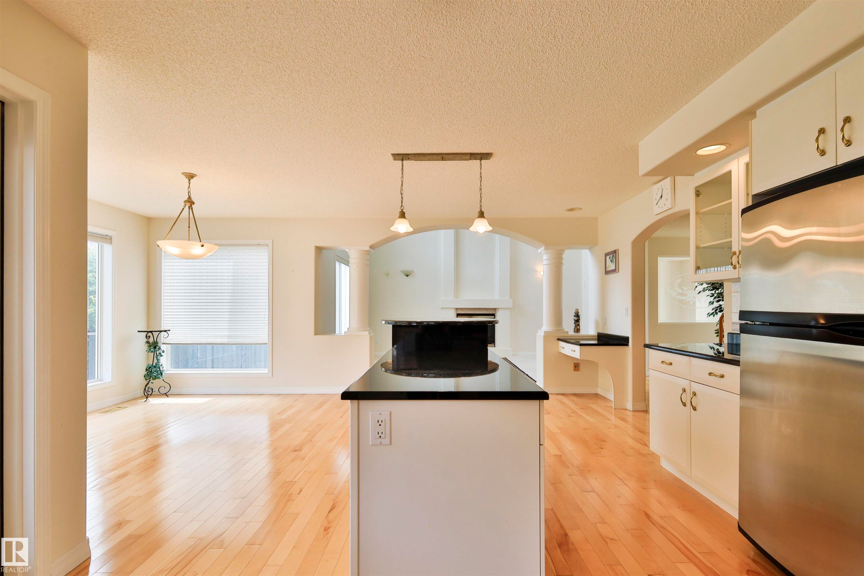 Spacious interior featuring wood-finish flooring, a kitchen island with pendant lighting, white cabinetry with brass hardware, stainless steel appliances, and arched doorways - 237 Darlington Crescent Nw, Edmonton, AB - Indoor Photo Showing Kitchen