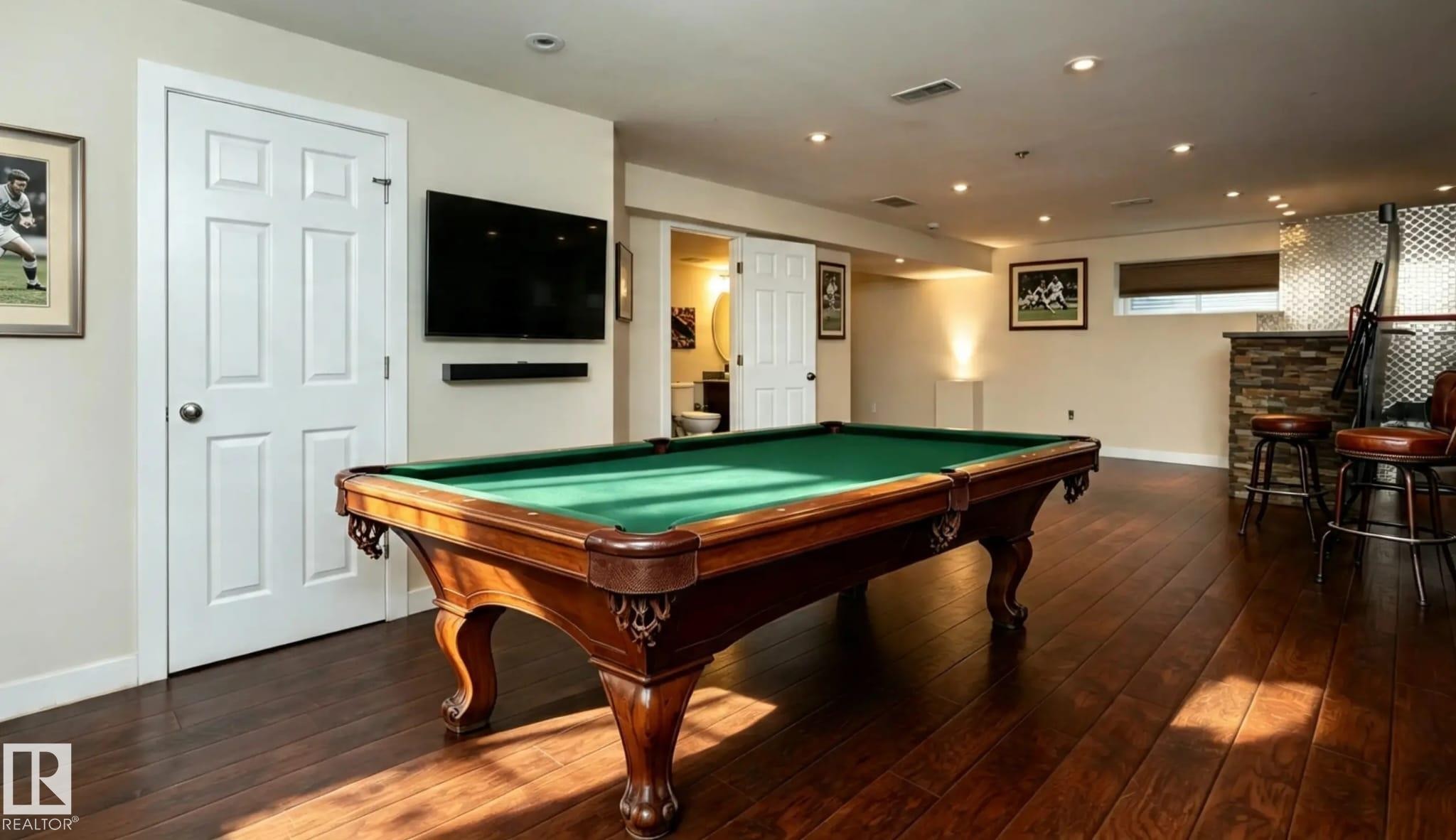 Hardwood-style flooring throughout, recessed ceiling lighting, built-in bar with stone-look facade, and a wall-mounted television - 16820 57 Street Nw, Edmonton, AB - Indoor Photo Showing Other Room