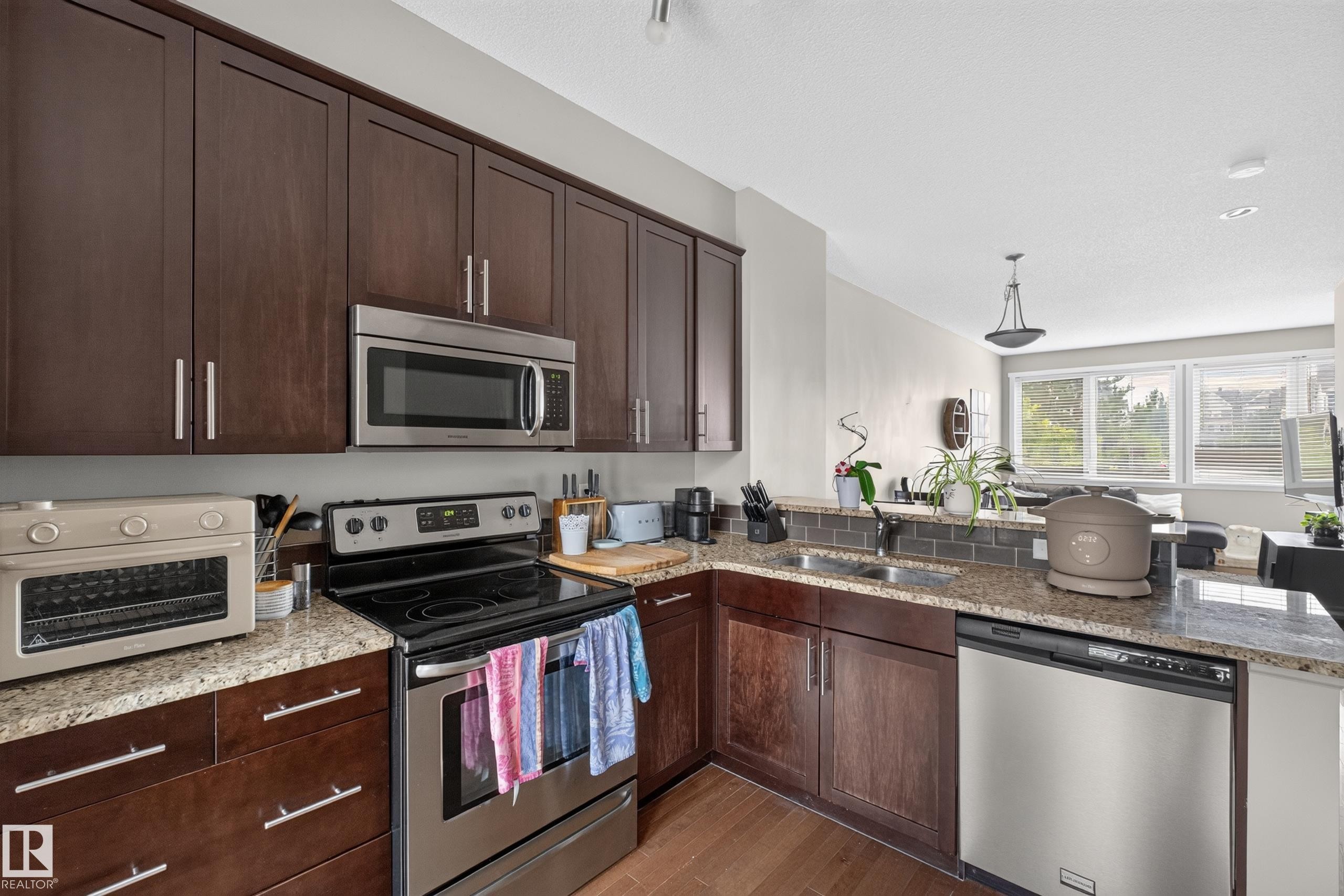 Kitchen featuring dark wood cabinetry, stainless steel appliances, and granite countertops - #53 603 Watt Bv Sw, Edmonton, AB - Indoor Photo Showing Kitchen With Double Sink