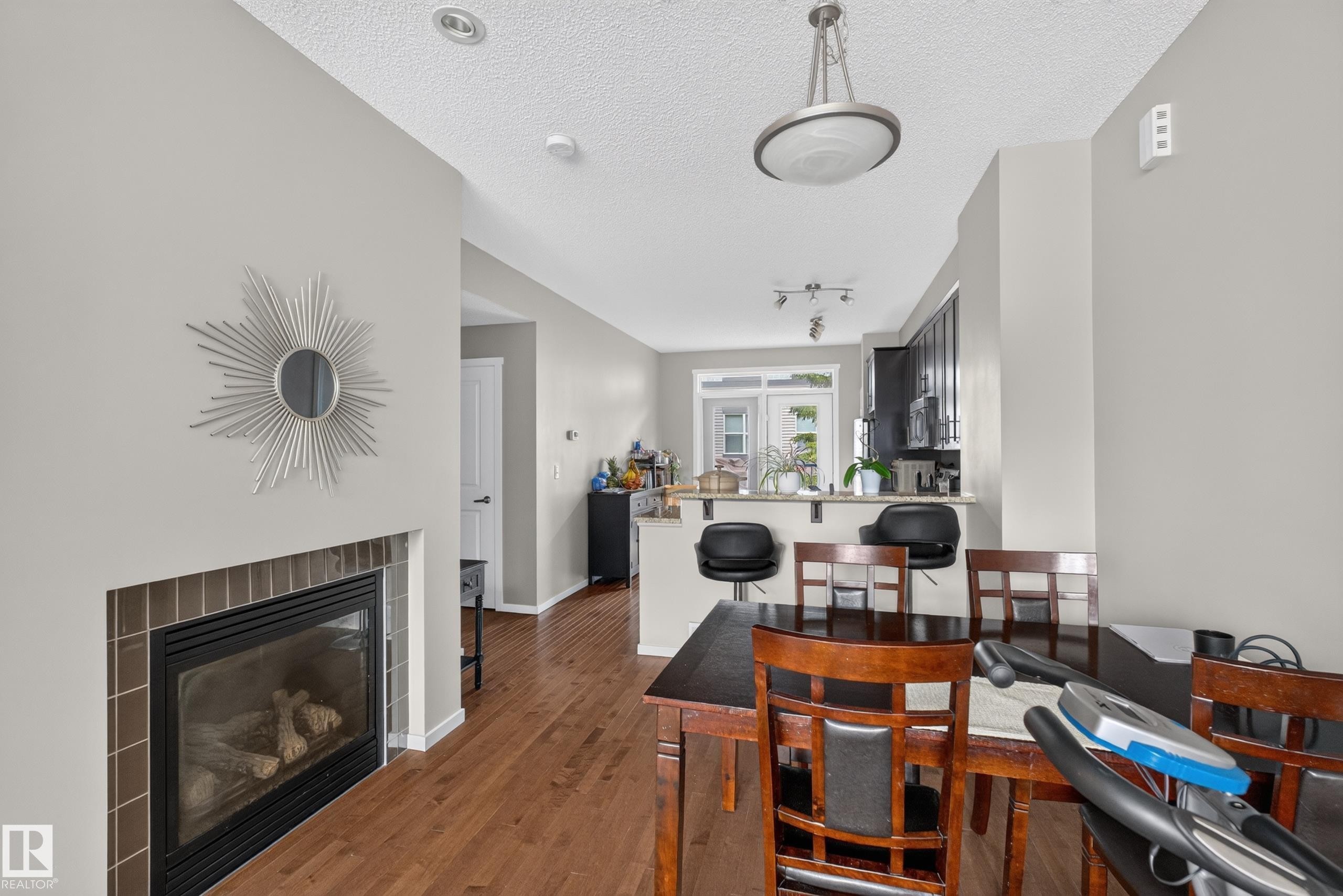 Fireplace with dark tile surround, featuring wood-finish flooring, recessed lighting, and a breakfast bar - #53 603 Watt Bv Sw, Edmonton, AB - Indoor With Fireplace