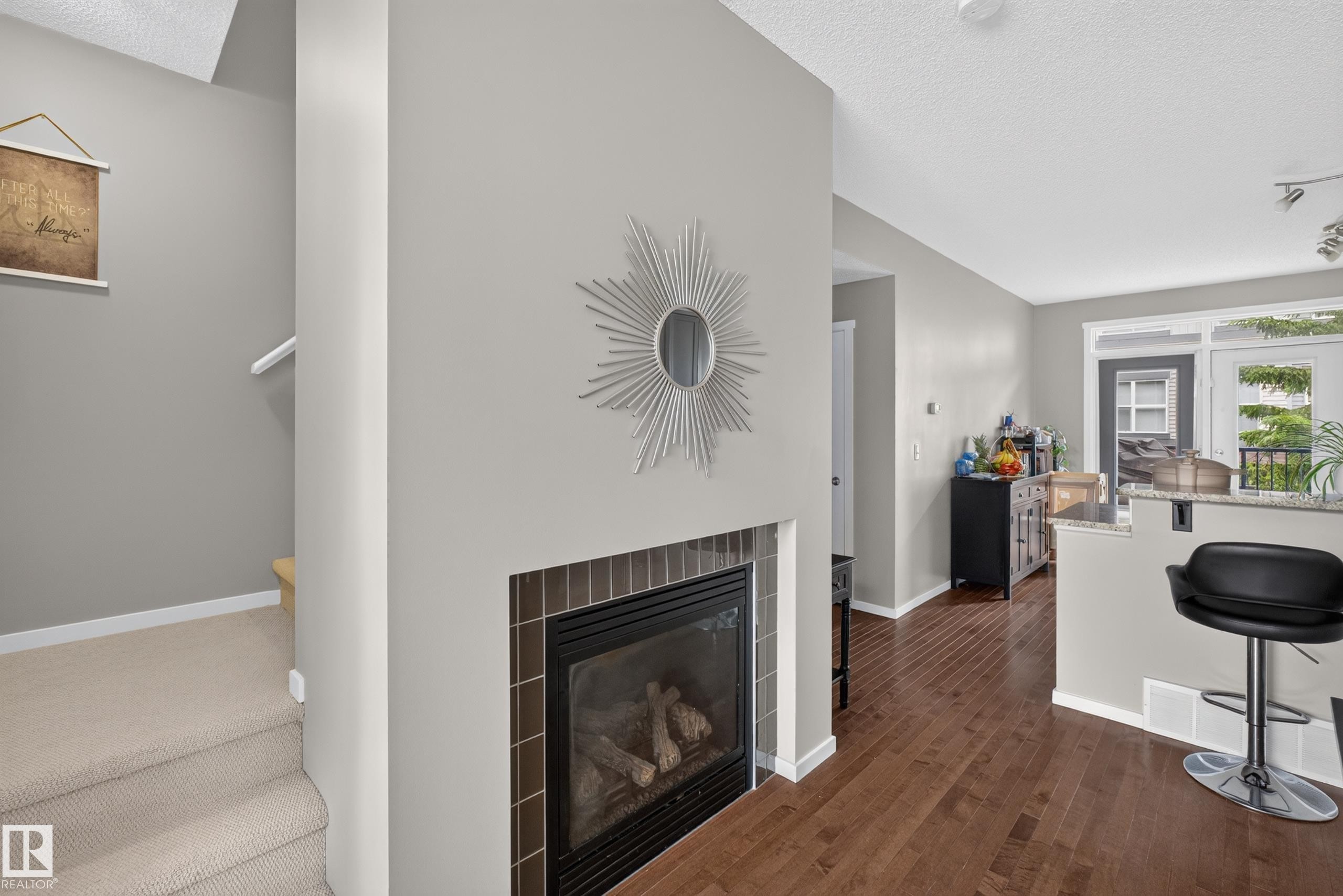 Gas fireplace with a tile surround, hardwood flooring, and a breakfast bar with a stone countertop - #53 603 Watt Bv Sw, Edmonton, AB - Indoor Photo Showing Living Room With Fireplace