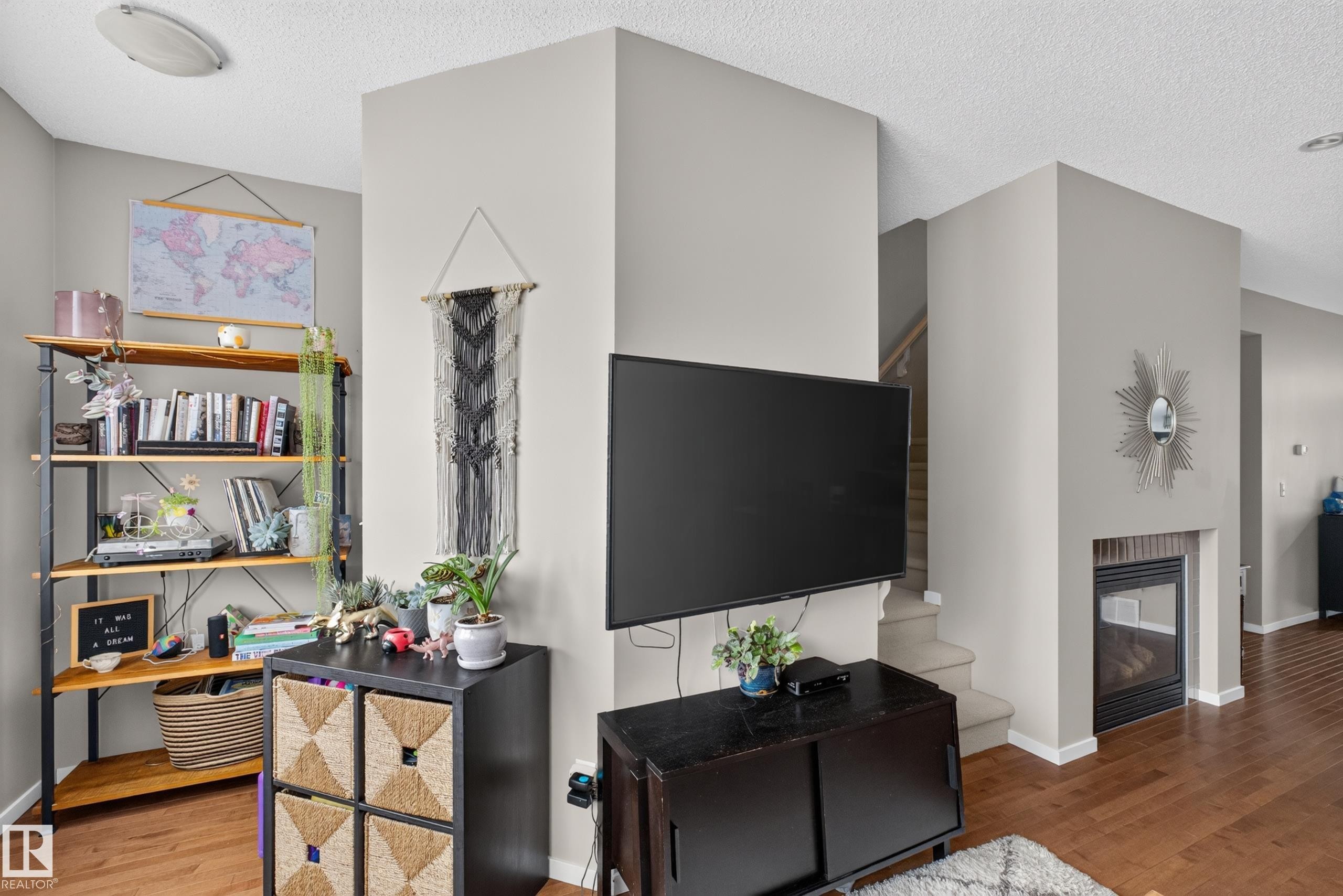 Living area with wood-finish flooring, light gray wall paint, and a built-in fireplace featuring a brick surround - #53 603 Watt Bv Sw, Edmonton, AB - Indoor