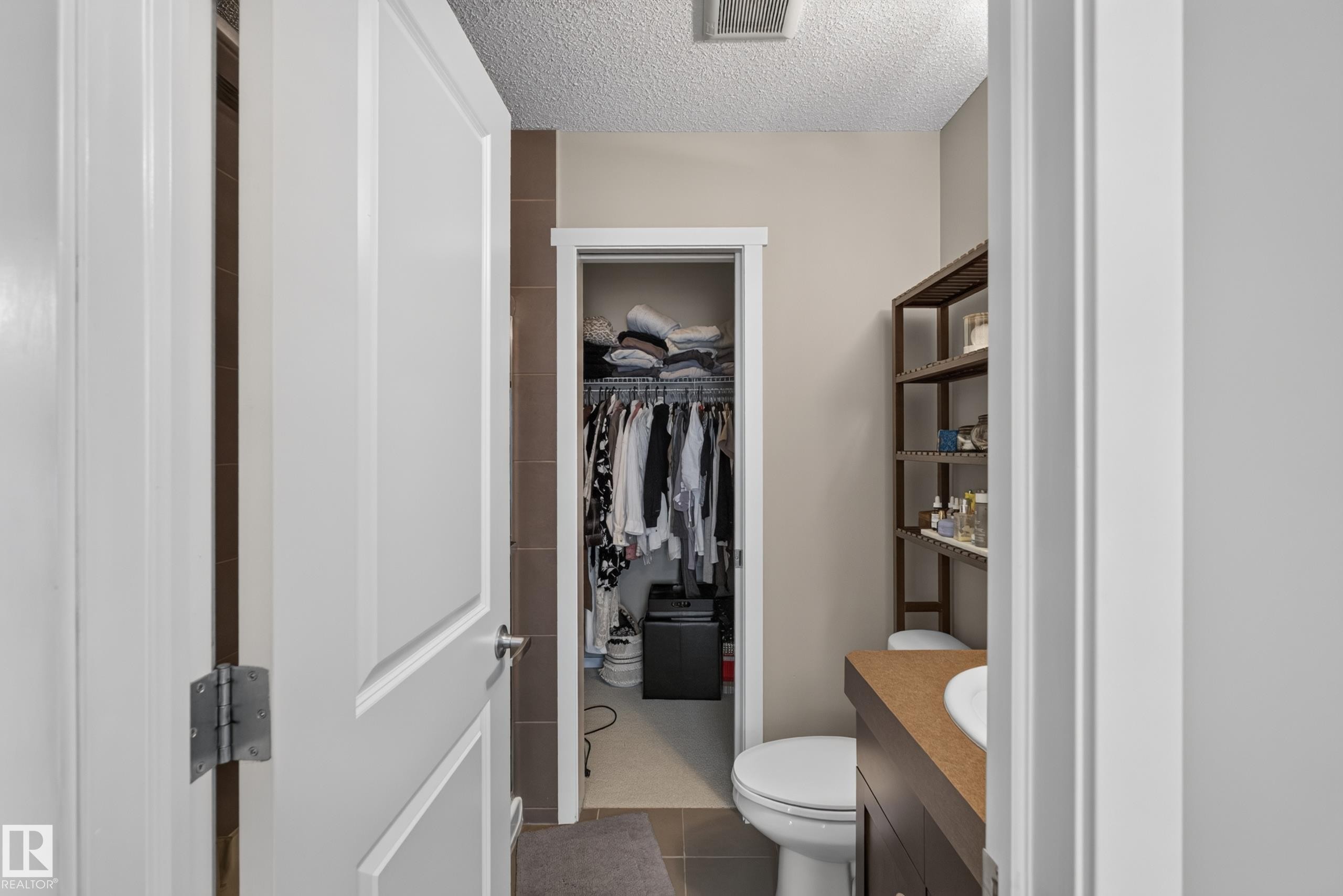 Bathroom featuring a built-in wood-finish vanity with an integrated sink, a toilet, and an open closet area with shelving and hanging storage - #53 603 Watt Bv Sw, Edmonton, AB - Indoor Photo Showing Bathroom