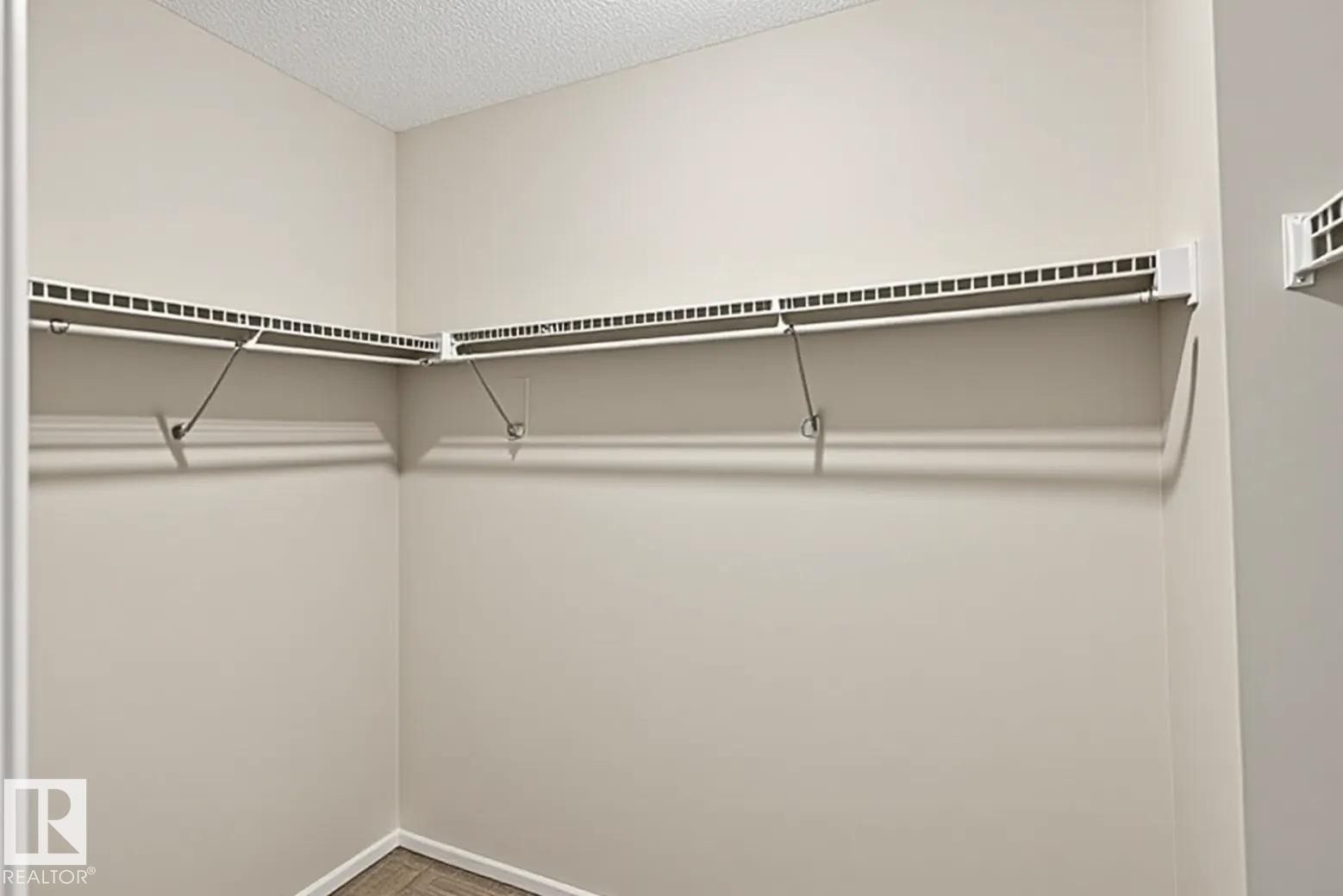 Built-in closet shelving system with white wire racks and hanging rods, beige wall paint, and wood-finish flooring - #53 603 Watt Bv Sw, Edmonton, AB - Indoor With Storage