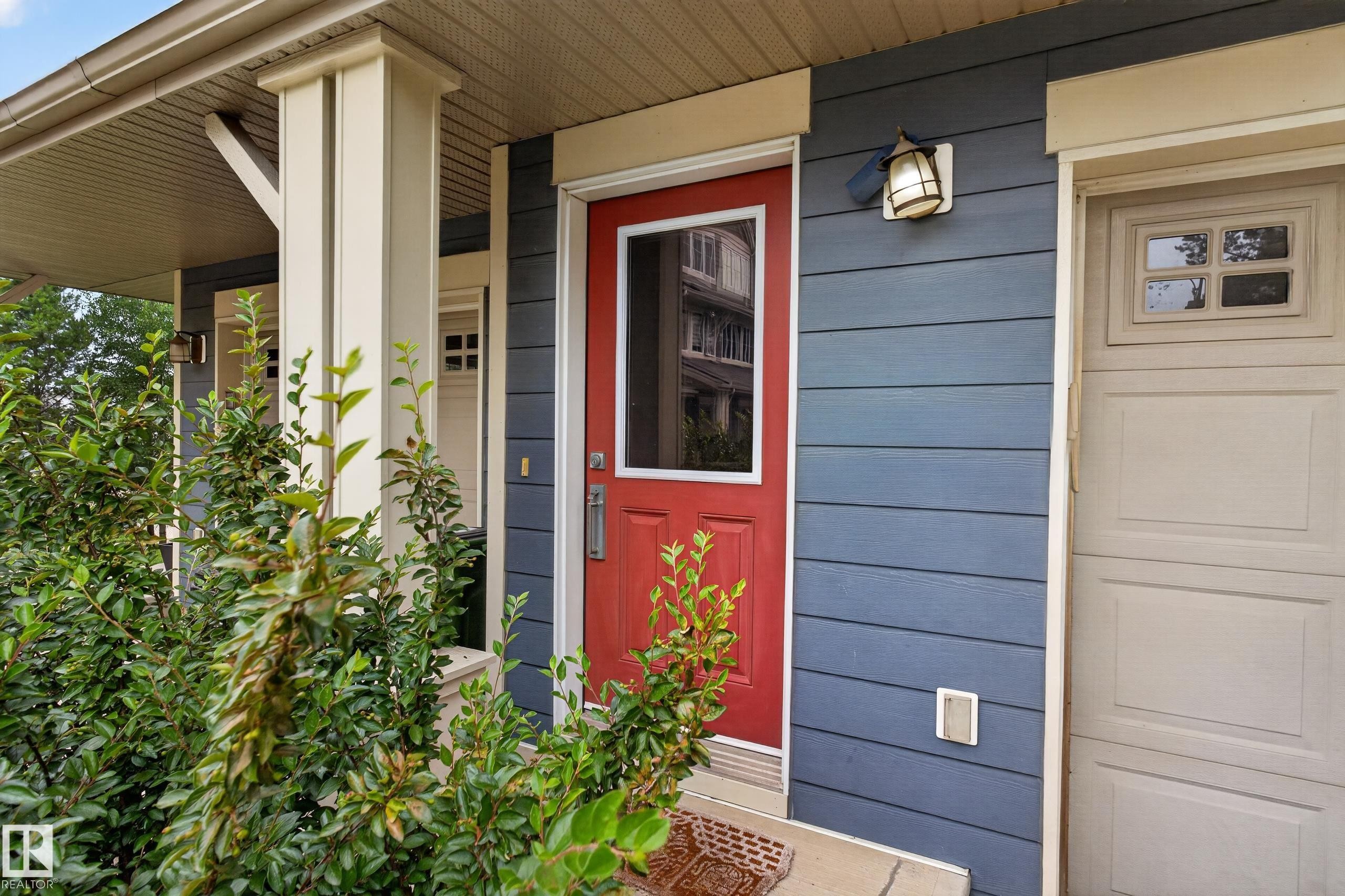 Vibrant red entry door with upper paneled glass, complemented by blue horizontal siding - #53 603 Watt Bv Sw, Edmonton, AB - Outdoor With Exterior