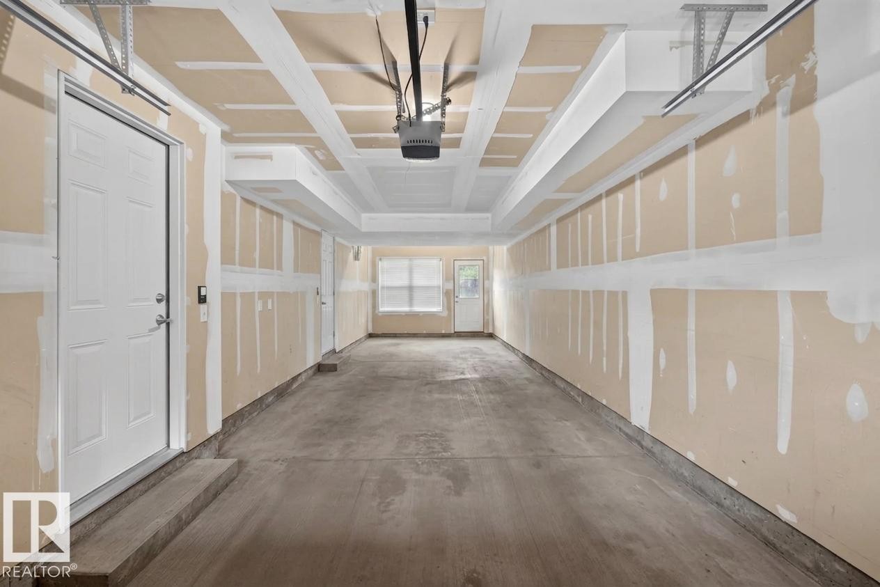 Spacious garage featuring a concrete floor, overhead door track system, and two white panel doors - #53 603 Watt Bv Sw, Edmonton, AB - Indoor Photo Showing Other Room